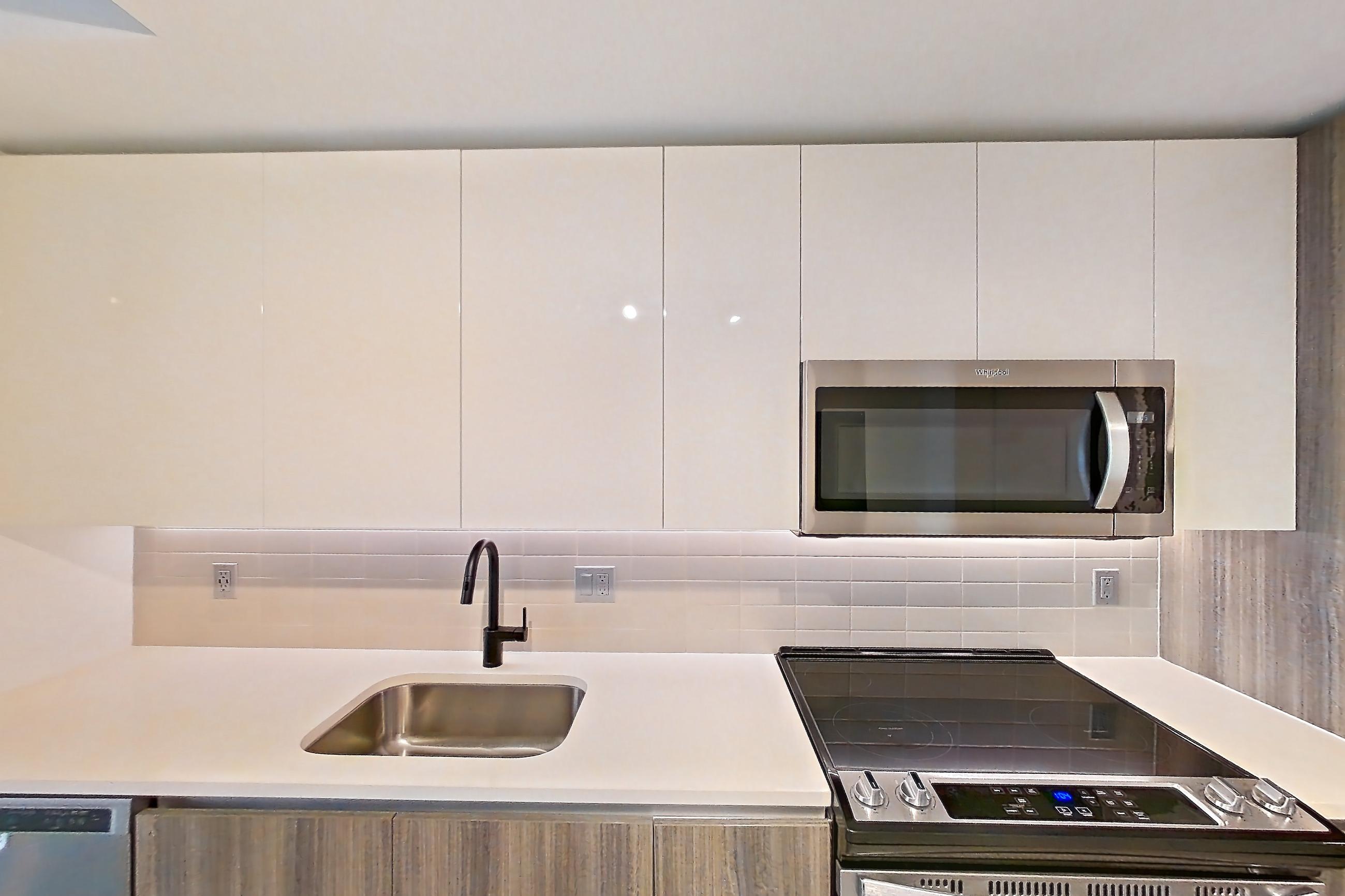 Kitchen with dishwasher, electric range, light countertops, light stone countertops, light tile flooring, light wood-finish flooring, microwave, oven/range, refrigerator, stainless steel appliances, water & ice dispenser, and wood-look tile flooring, Apartment 2518 at Cortland Midtown Miami