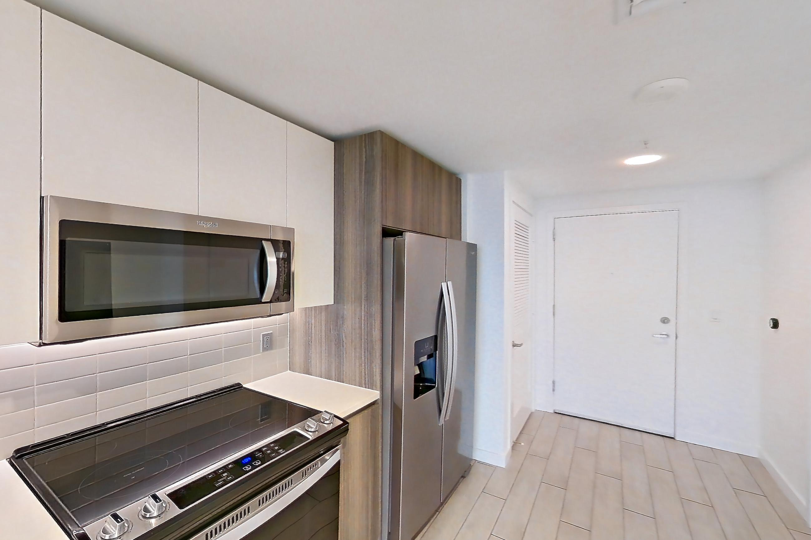Kitchen with dishwasher, electric range, light countertops, light stone countertops, light tile flooring, light wood-finish flooring, microwave, oven/range, refrigerator, stainless steel appliances, water & ice dispenser, and wood-look tile flooring, Apartment 2518 at Cortland Midtown Miami