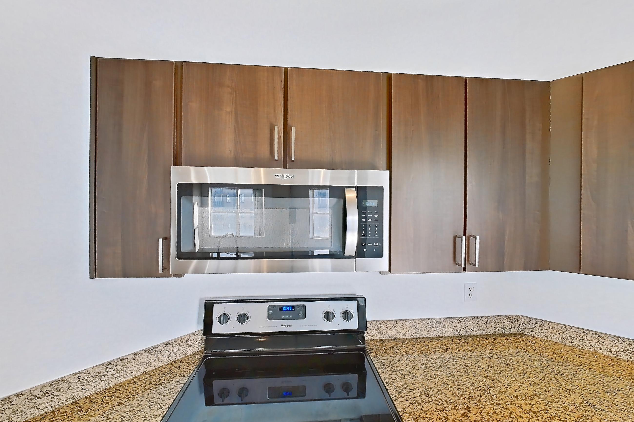 Kitchen with dishwasher, electric range, light stone countertops, light wood-finish flooring, microwave, oven/range, refrigerator, stainless steel appliances, and white appliances, Apartment 1430 at Cortland on Blake