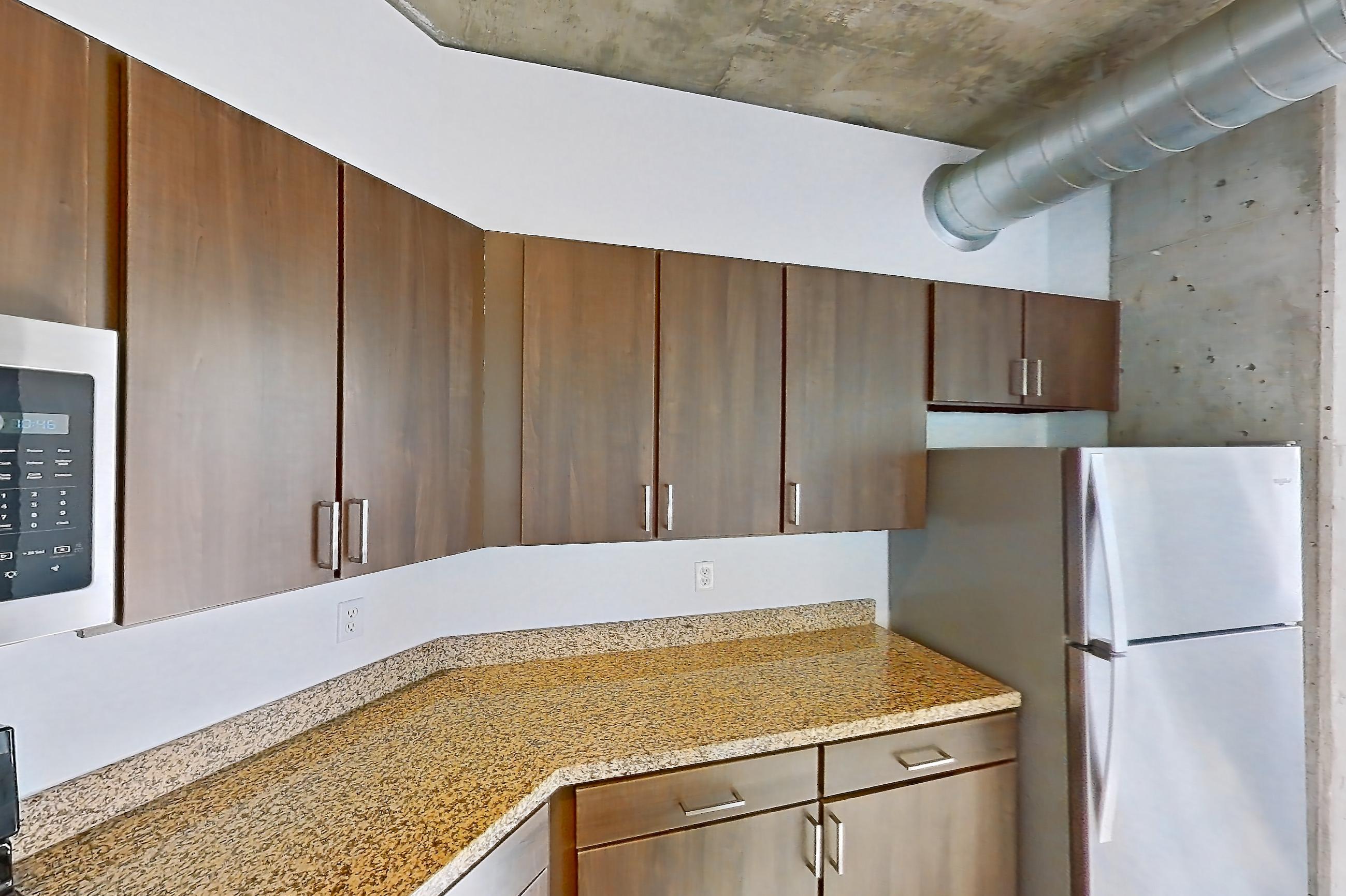 Kitchen with dishwasher, electric range, light stone countertops, light wood-finish flooring, microwave, oven/range, refrigerator, stainless steel appliances, and white appliances, Apartment 1430 at Cortland on Blake