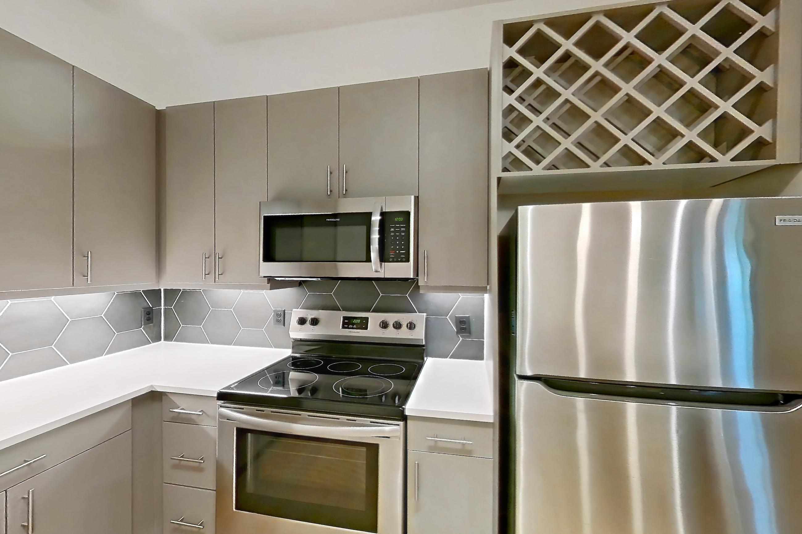 Kitchen with electric range, light countertops, light wood-finish flooring, oven/range, refrigerator, and stainless steel appliances, Apartment 7408 at Cortland Satori