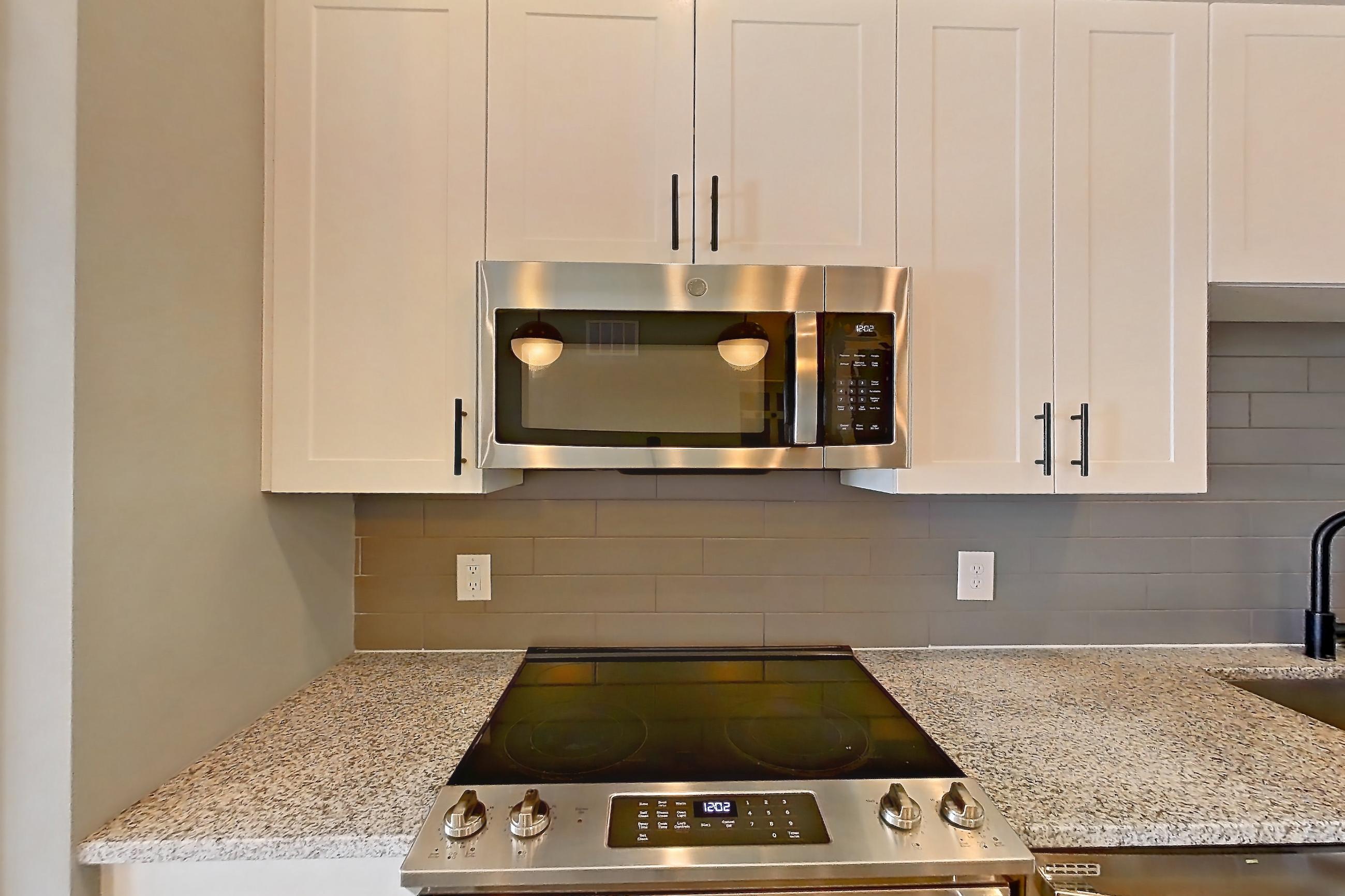 Kitchen with dishwasher, electric range, light countertops, light stone countertops, light wood-finish flooring, microwave, oven/range, refrigerator, stainless steel appliances, and water & ice dispenser, Apartment 2-135 at Cortland Cary