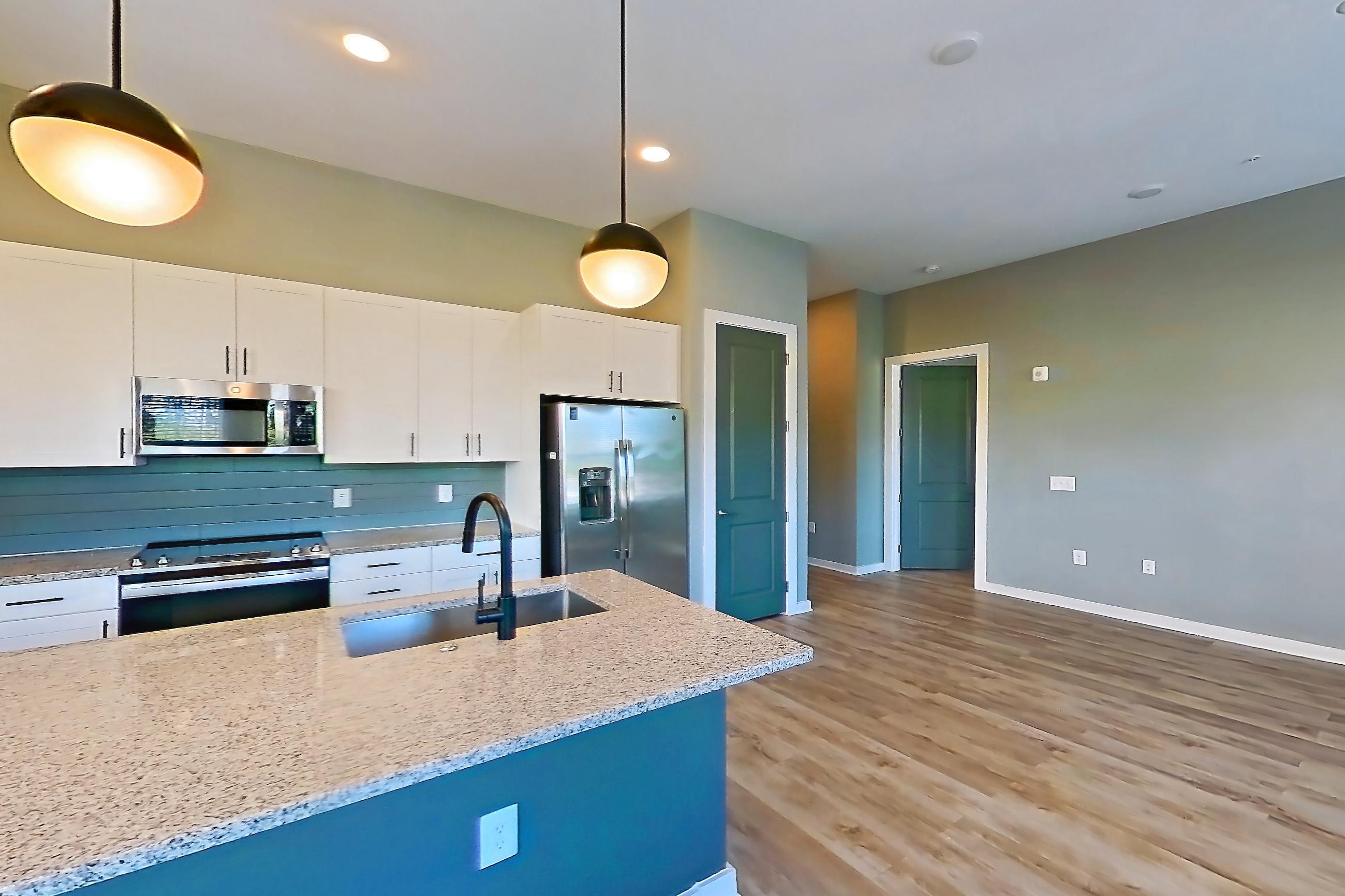 Dining room with electric range, kitchen island, light countertops, light stone countertops, light wood-finish flooring, microwave, oven/range, refrigerator, stainless steel appliances, and water & ice dispenser, Apartment 2-132 at Cortland Cary