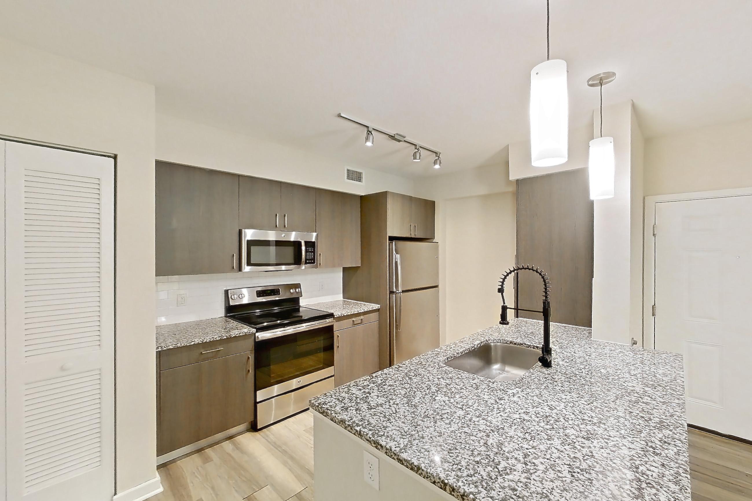 Kitchen entryway with electric range, kitchen island, light countertops, light stone countertops, light wood-finish flooring, oven/range, refrigerator, and stainless steel appliances, Apartment 01104 at Cortland Hollywood