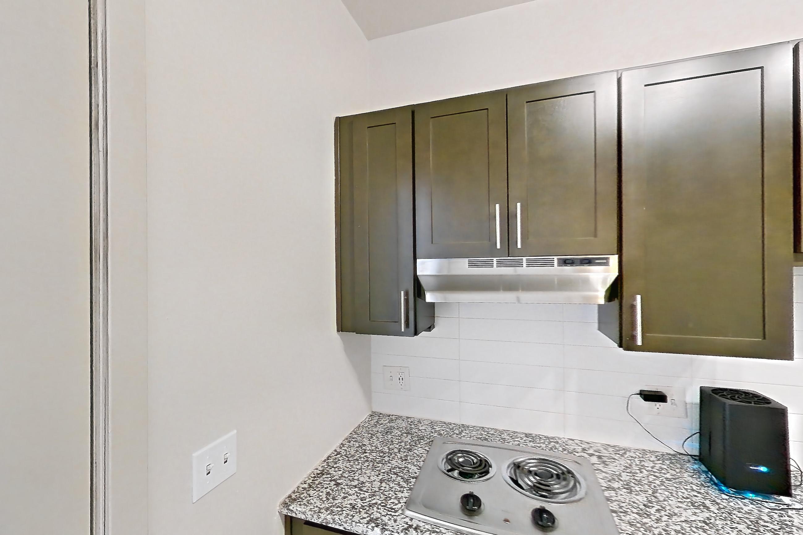 Kitchen with cooktop, dark wood-finish flooring, dishwasher, electric cooktop, light stone countertops, microwave, oven/range, refrigerator, and stainless steel appliances, Apartment N102A at Cortland Alameda Station