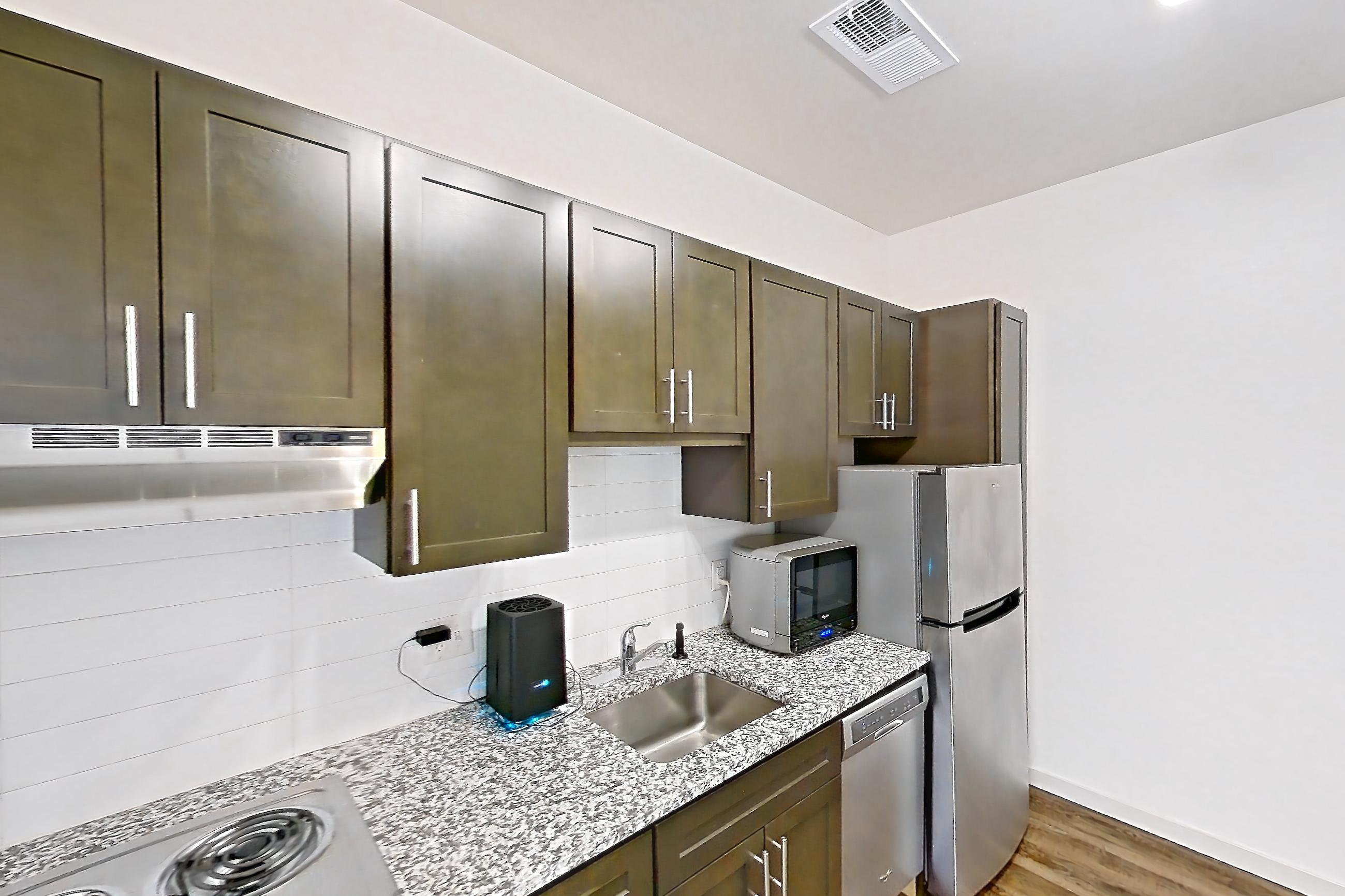 Kitchen with cooktop, dark wood-finish flooring, dishwasher, electric cooktop, light stone countertops, microwave, oven/range, refrigerator, and stainless steel appliances, Apartment N102A at Cortland Alameda Station