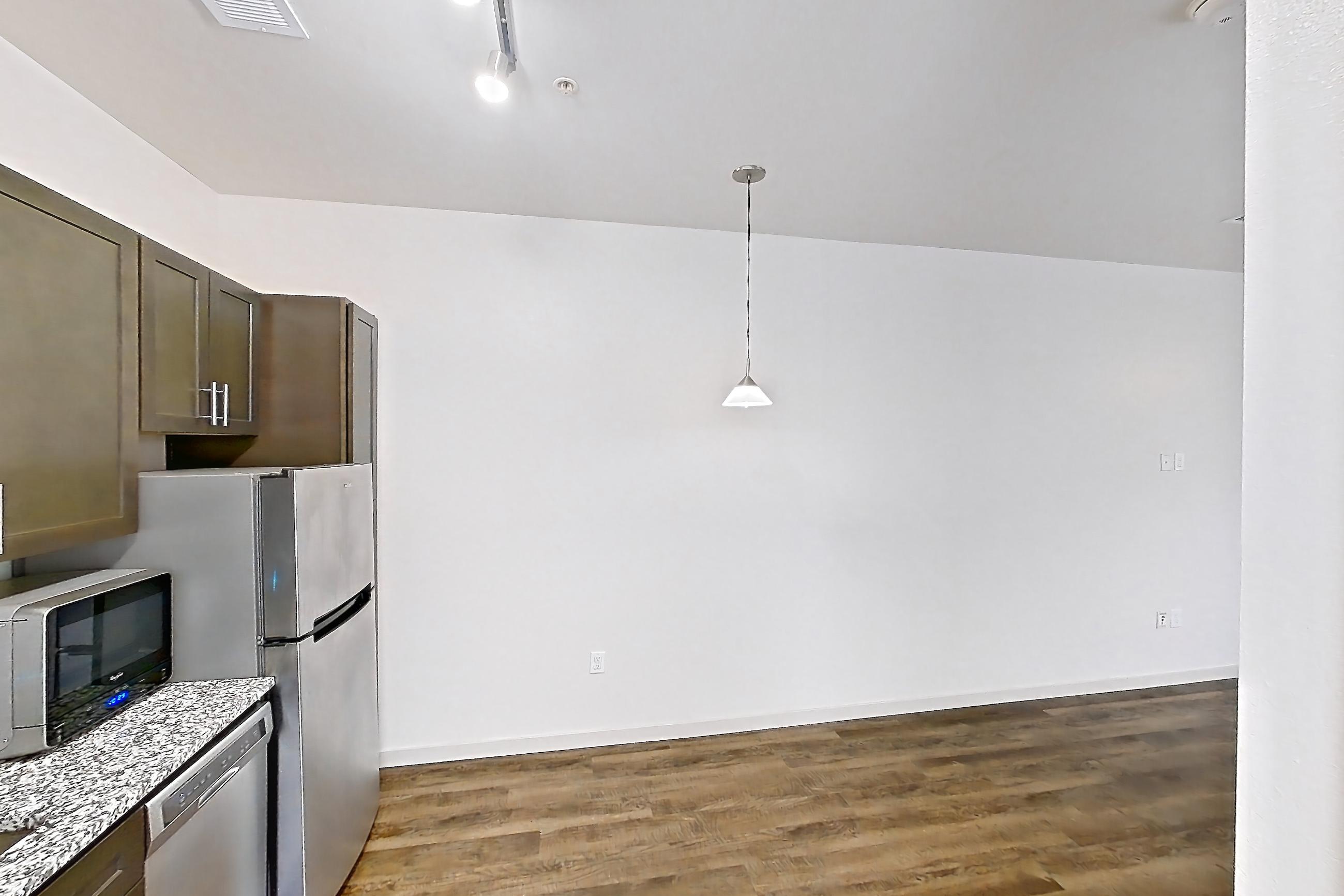 Kitchen with cooktop, dark wood-finish flooring, dishwasher, electric cooktop, light stone countertops, microwave, oven/range, refrigerator, and stainless steel appliances, Apartment N102A at Cortland Alameda Station