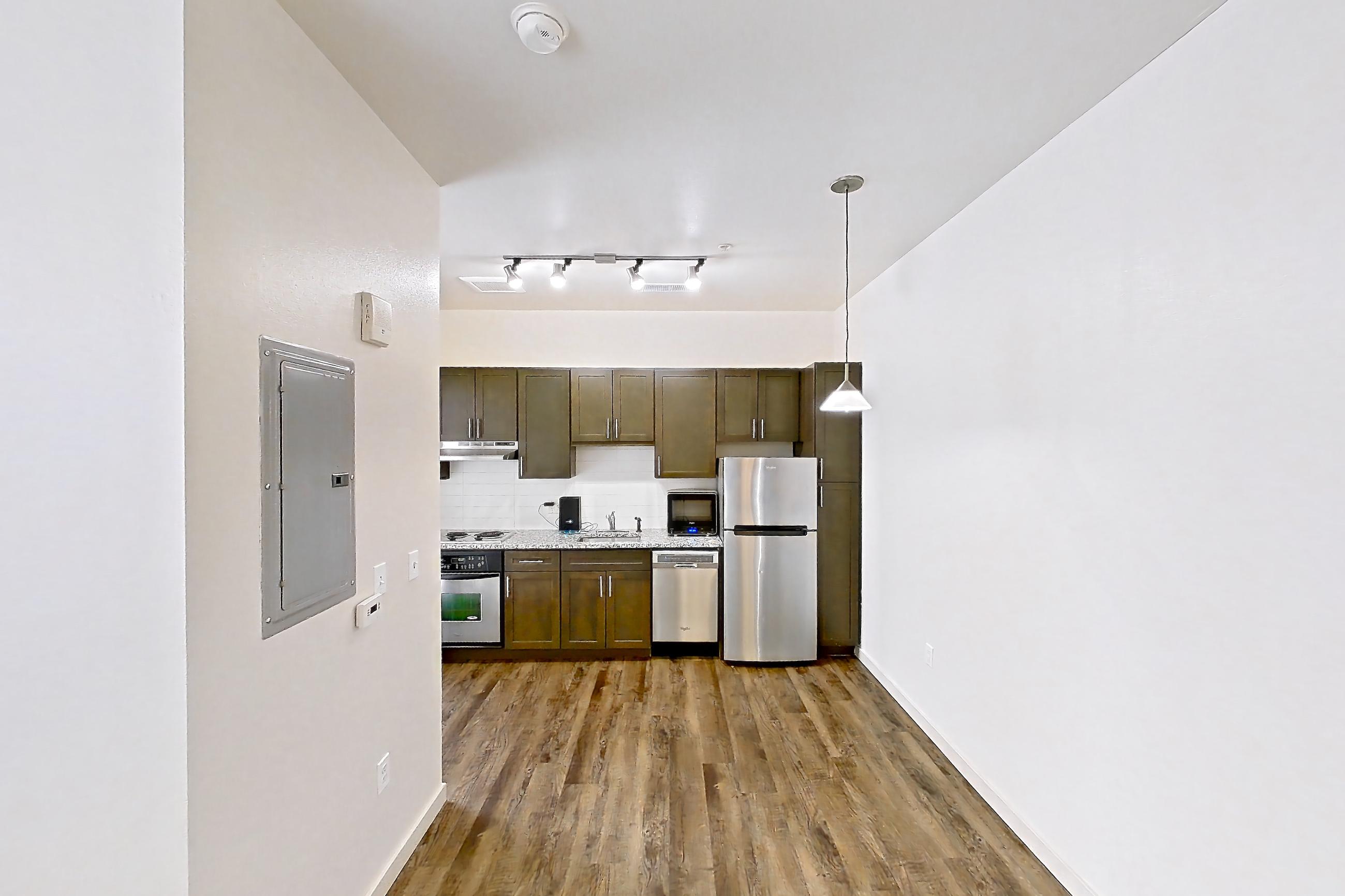 Living space with cooktop, dark wood-finish flooring, dishwasher, light stone countertops, oven/range, refrigerator, and stainless steel appliances, Apartment N102A at Cortland Alameda Station