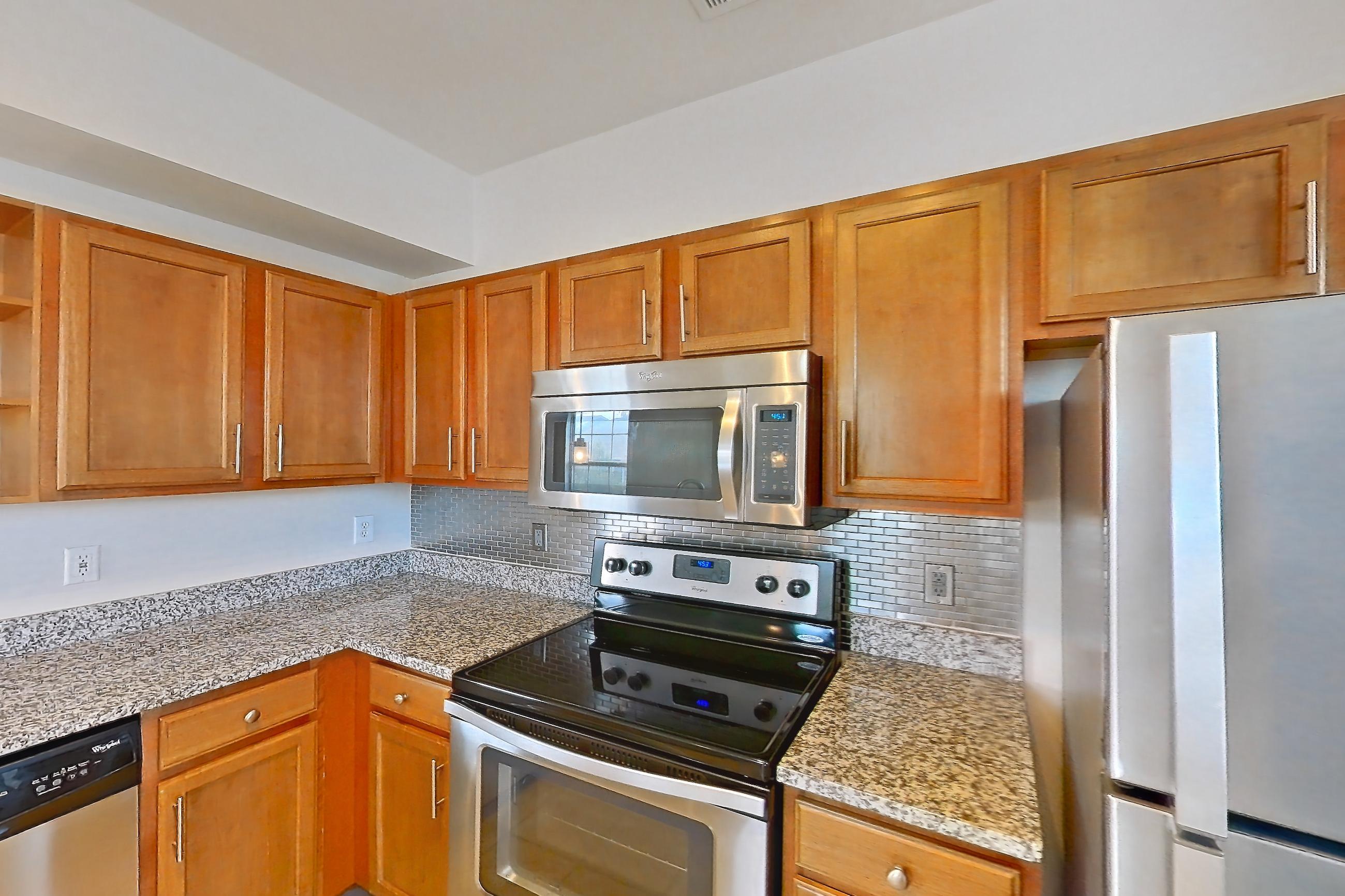 Kitchen with dishwasher, electric range, light carpet, light countertops, light stone countertops, light tile flooring, microwave, oven/range, refrigerator, and stainless steel appliances, Apartment 1-939 at Cortland Ridglea