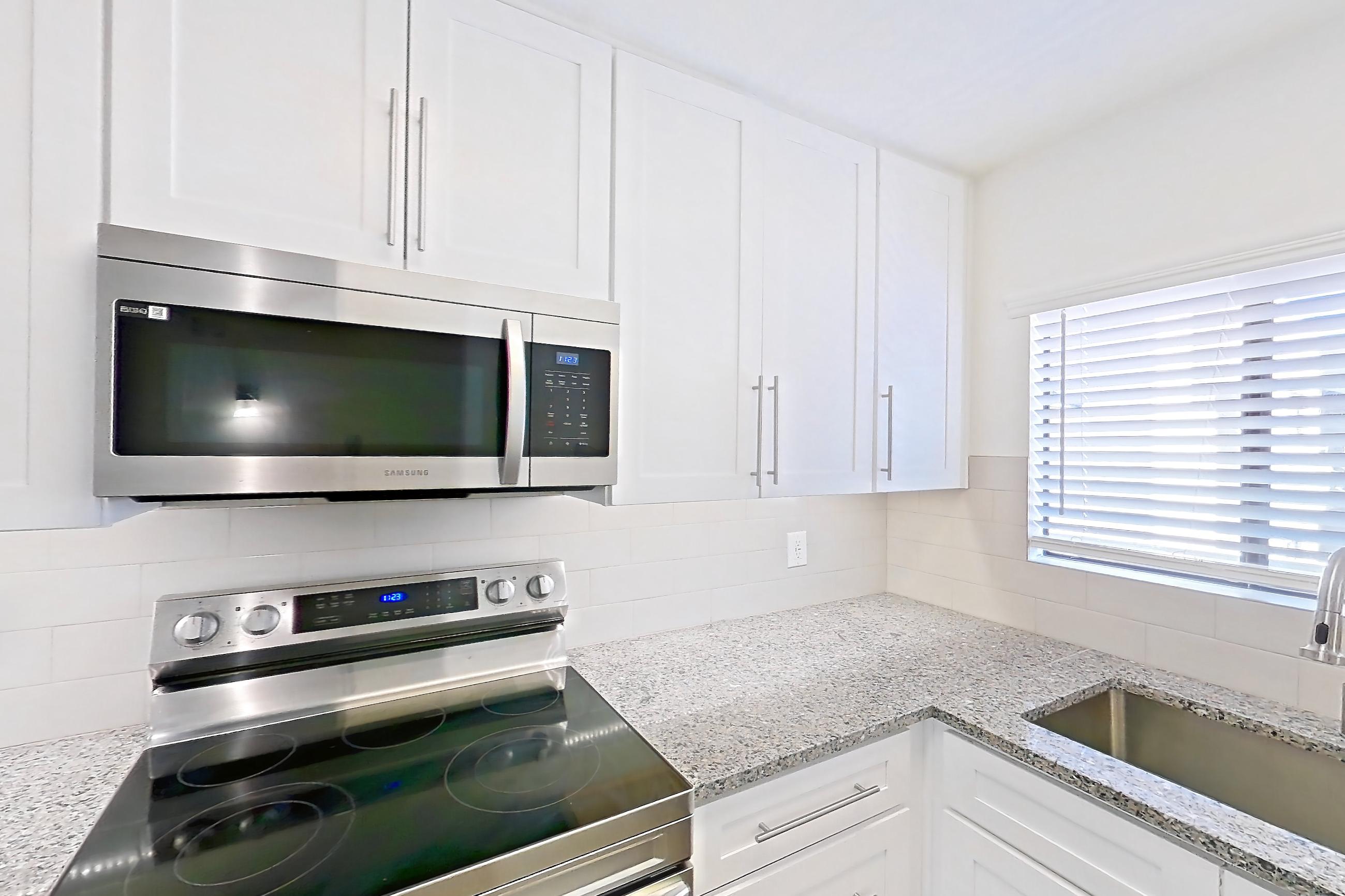 Kitchen with dishwasher, electric range, light countertops, light stone countertops, light wood-finish flooring, microwave, oven/range, range hood, refrigerator, and stainless steel appliances, Apartment 19289 at Cortland Sabino Canyon
