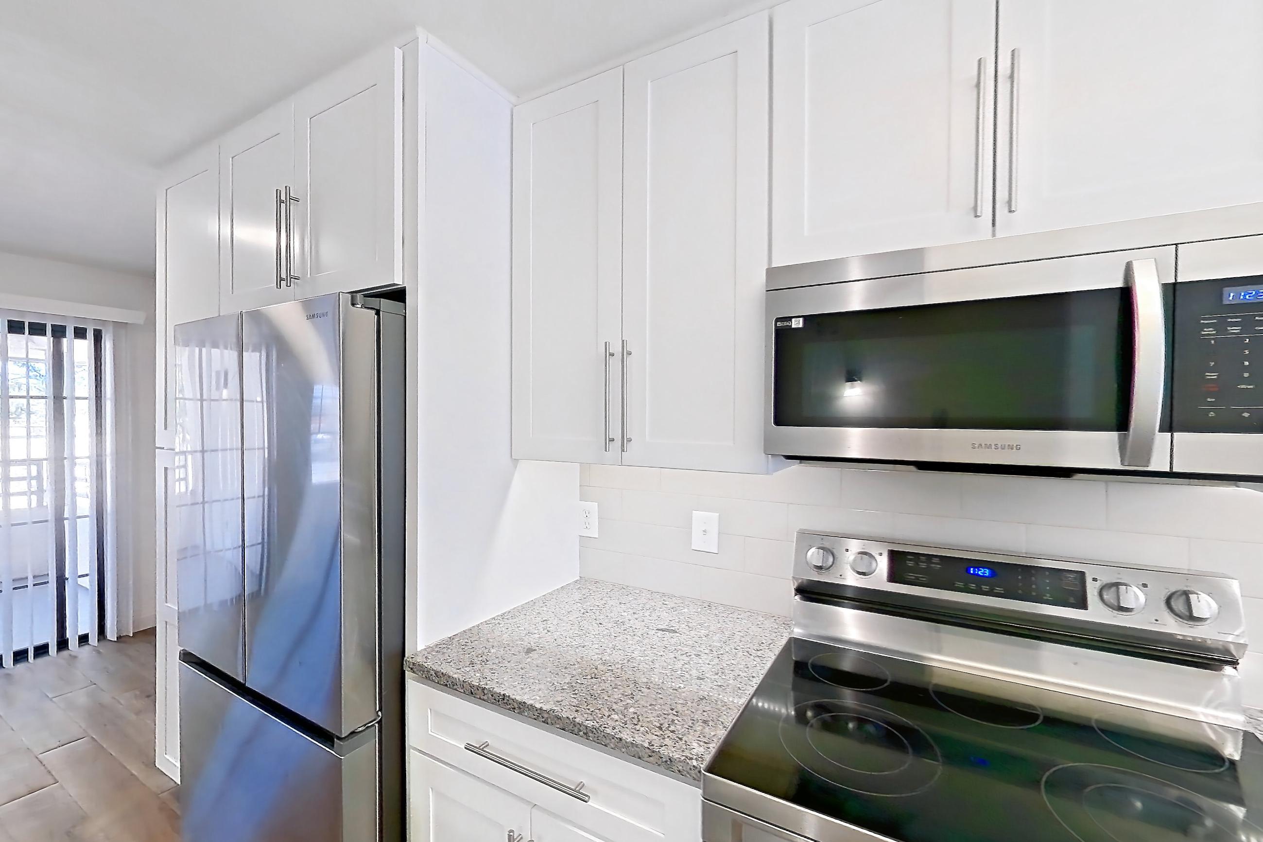 Kitchen with dishwasher, electric range, light countertops, light stone countertops, light wood-finish flooring, microwave, oven/range, range hood, refrigerator, and stainless steel appliances, Apartment 19289 at Cortland Sabino Canyon