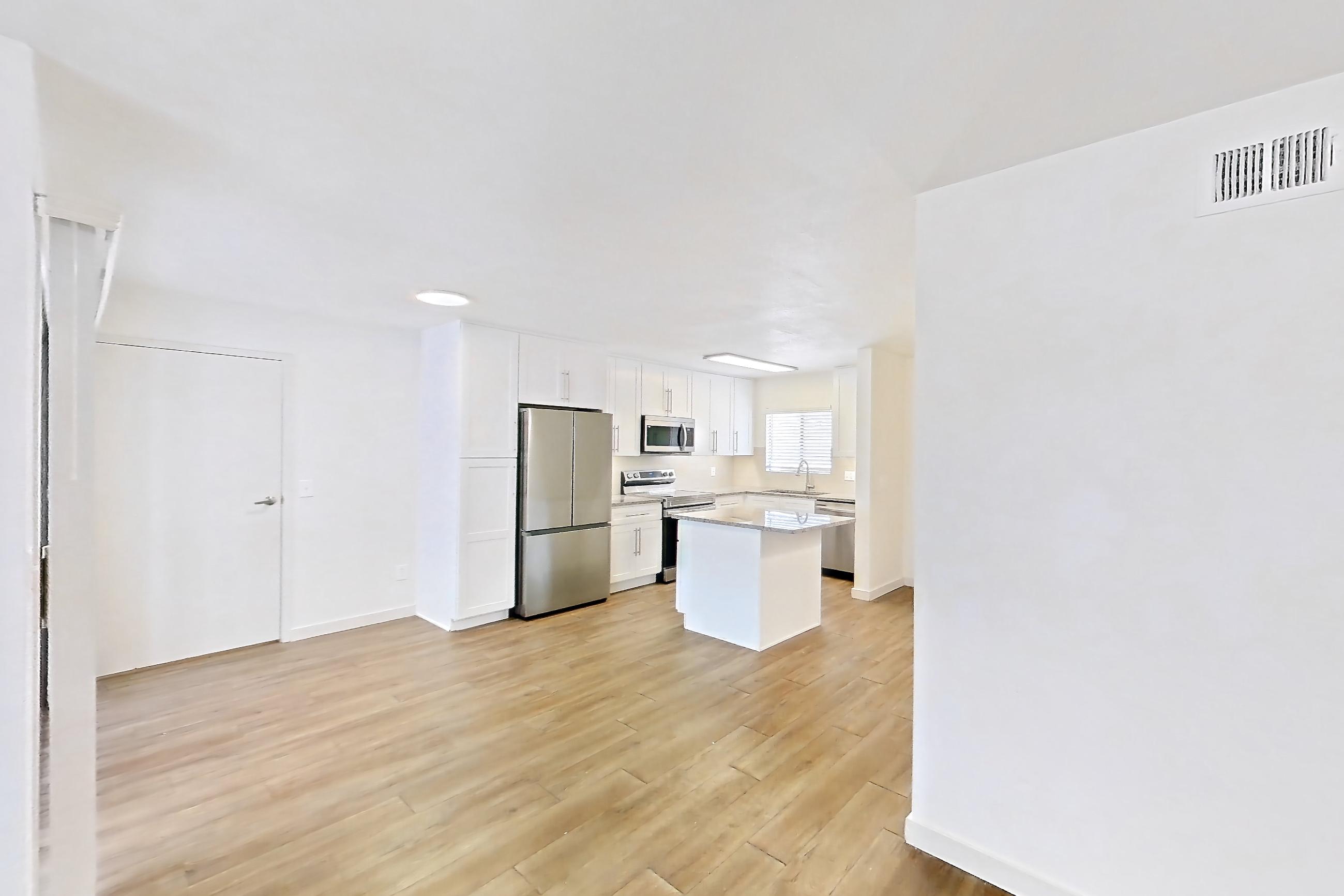 Living room with dark wood-finish flooring, light stone countertops, light wood-finish flooring, refrigerator, and stainless steel appliances, Apartment 19289 at Cortland Sabino Canyon