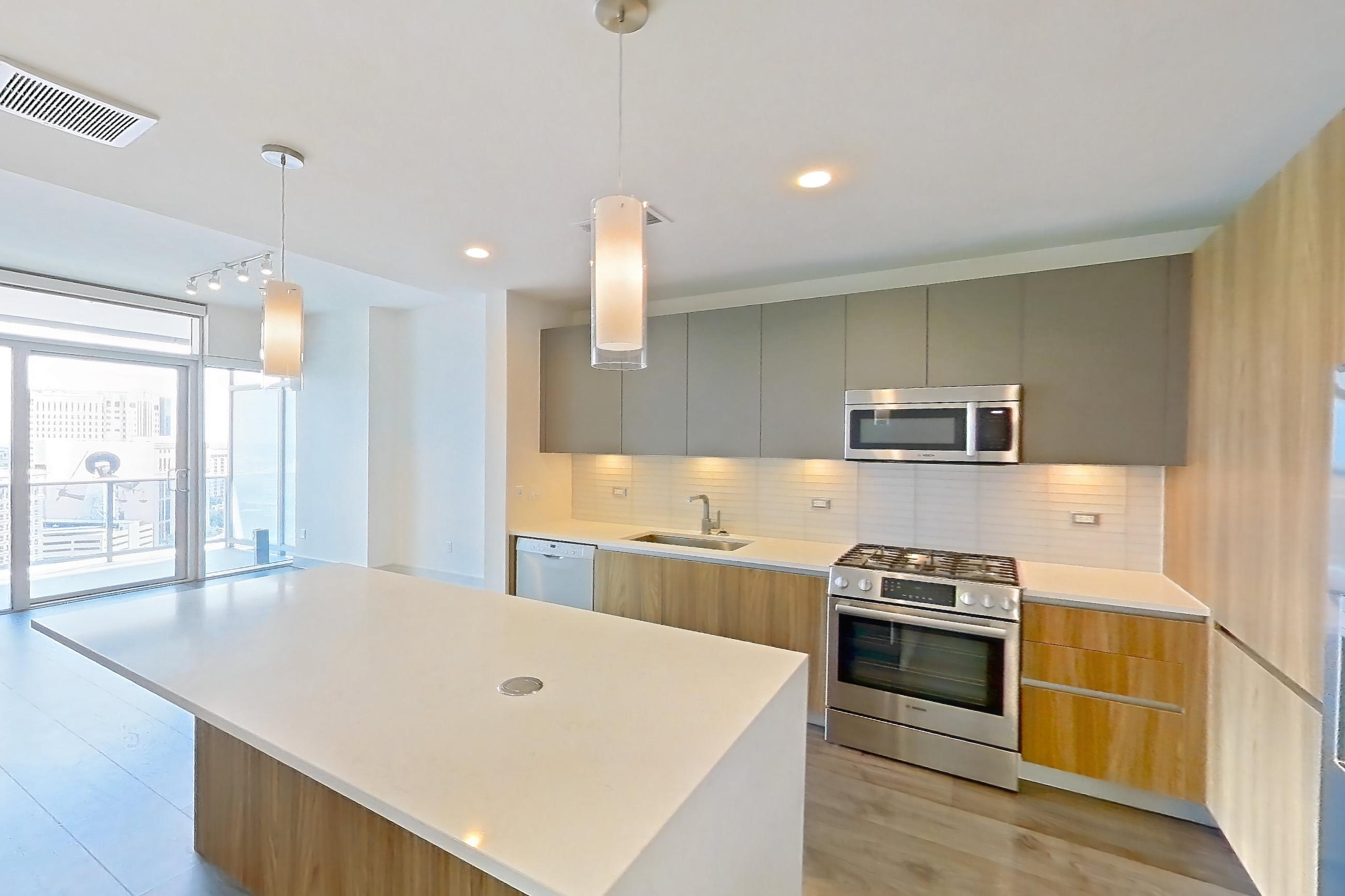Living space with dark wood-finish flooring, dishwasher, gas range, light stone countertops, microwave, oven/range, refrigerator, stainless steel appliances, water & ice dispenser, white appliances, and wood-finish flooring, Apartment 2006 at Brava