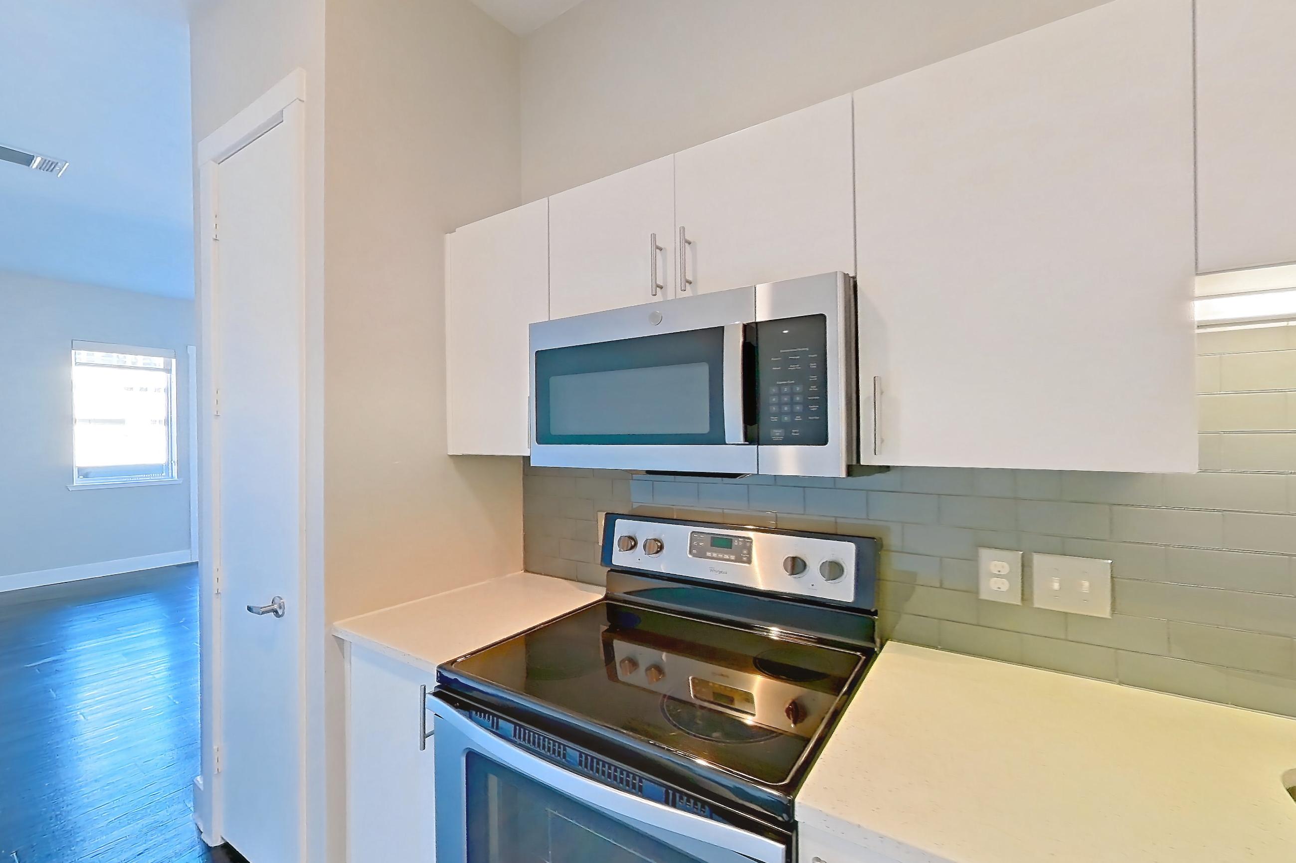 Kitchen with dark wood-finish flooring, dishwasher, electric range, light countertops, microwave, oven/range, stainless steel appliances, and wood-finish flooring, Unit 259 at Harvest Lofts