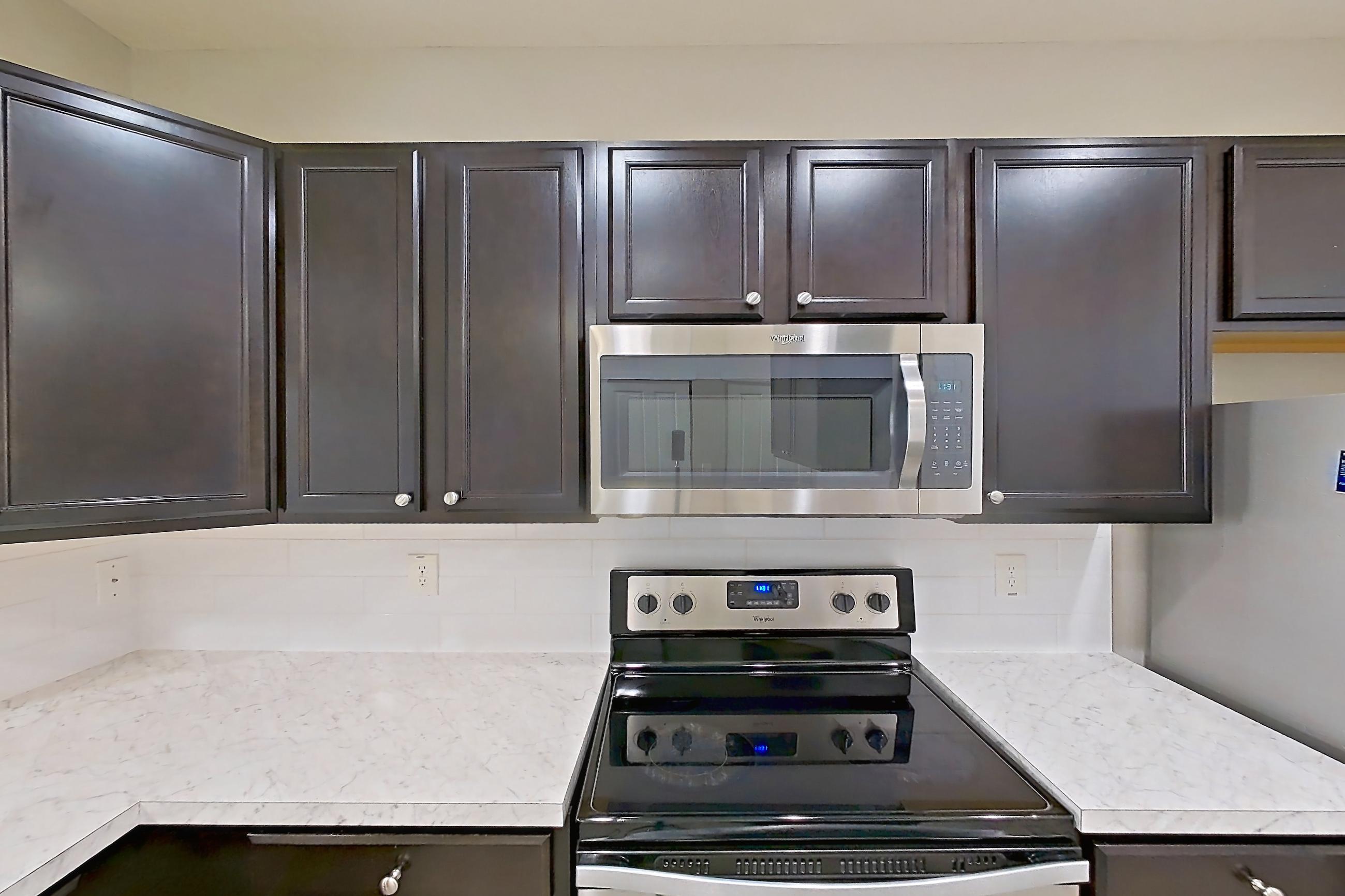 Kitchen with dishwasher, electric range, light countertops, light wood-finish flooring, microwave, oven/range, refrigerator, stainless steel appliances, and white appliances, Apartment C3318 at Cortland Powell