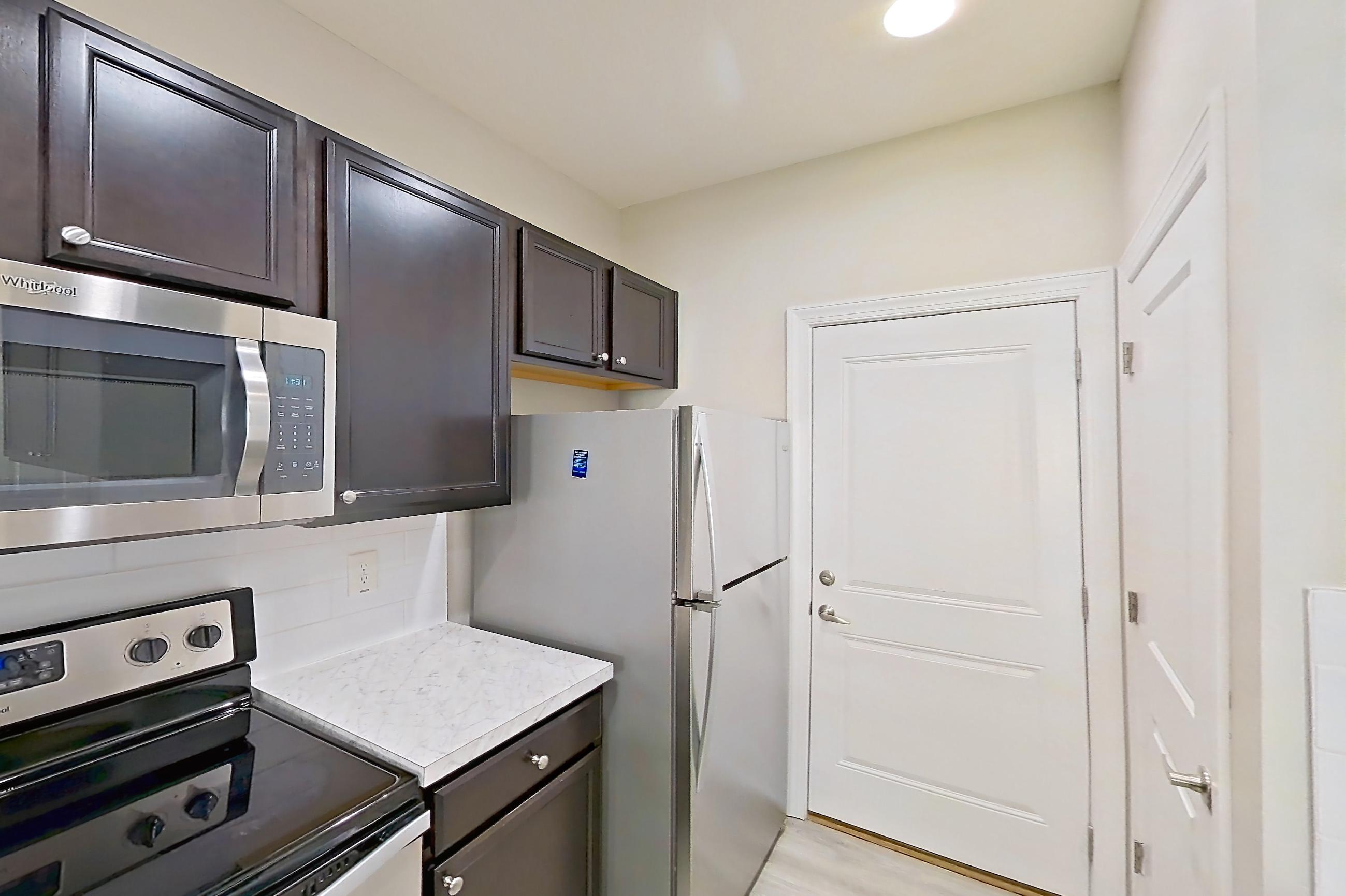 Kitchen with dishwasher, electric range, light countertops, light wood-finish flooring, microwave, oven/range, refrigerator, stainless steel appliances, and white appliances, Apartment C3318 at Cortland Powell