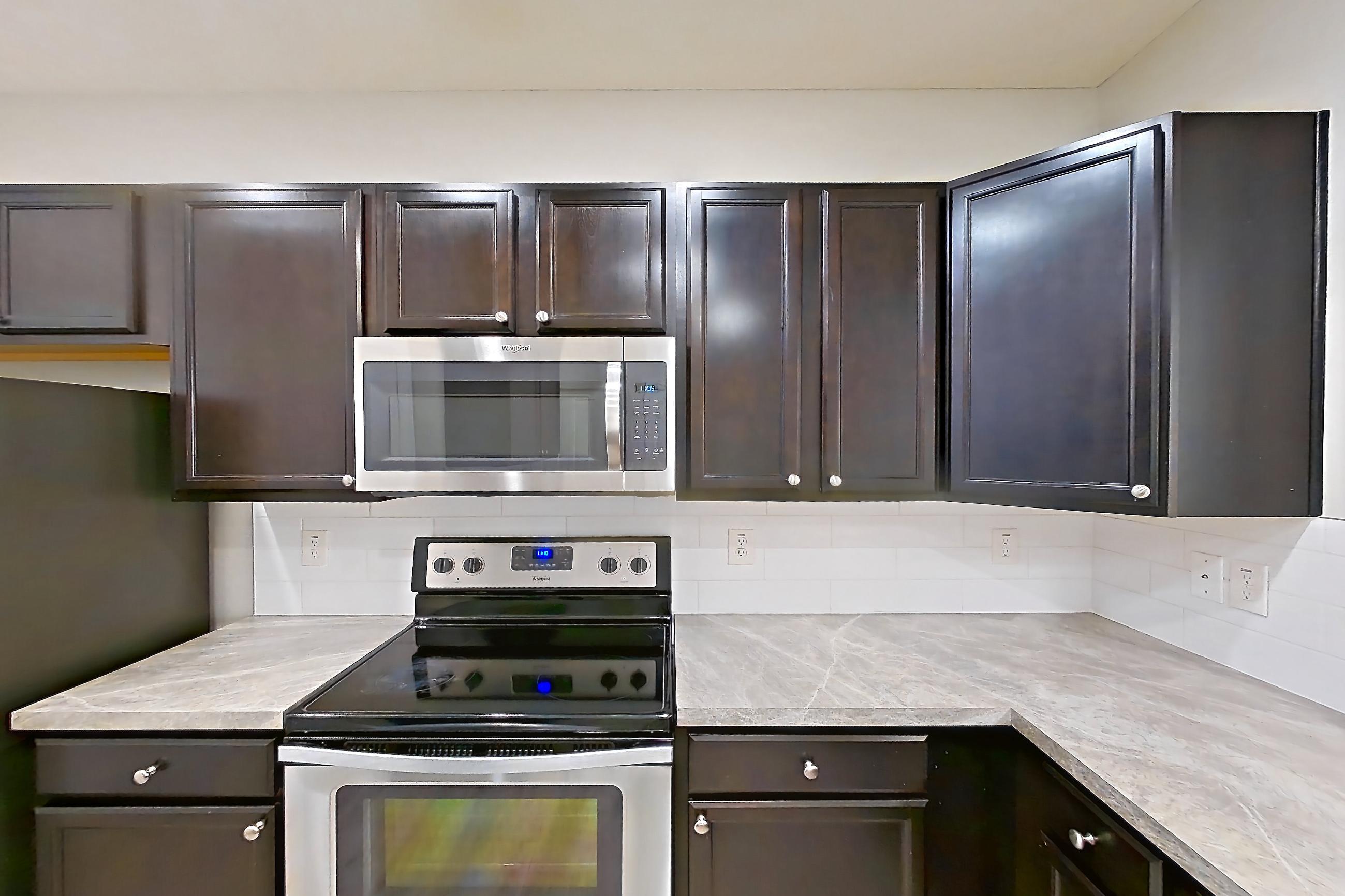 Kitchen with dishwasher, electric range, light countertops, light wood-finish flooring, microwave, oven/range, refrigerator, and stainless steel appliances, Apartment M3271 at Cortland Powell