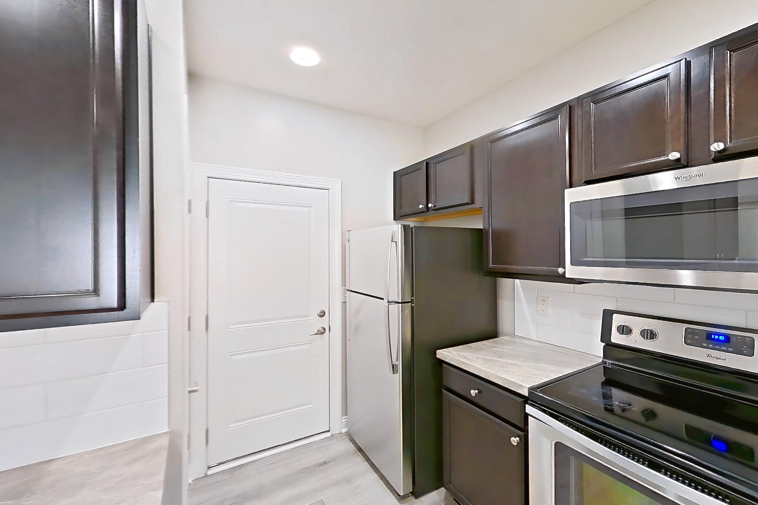 Kitchen with dishwasher, electric range, light countertops, light wood-finish flooring, microwave, oven/range, refrigerator, and stainless steel appliances, Apartment M3271 at Cortland Powell