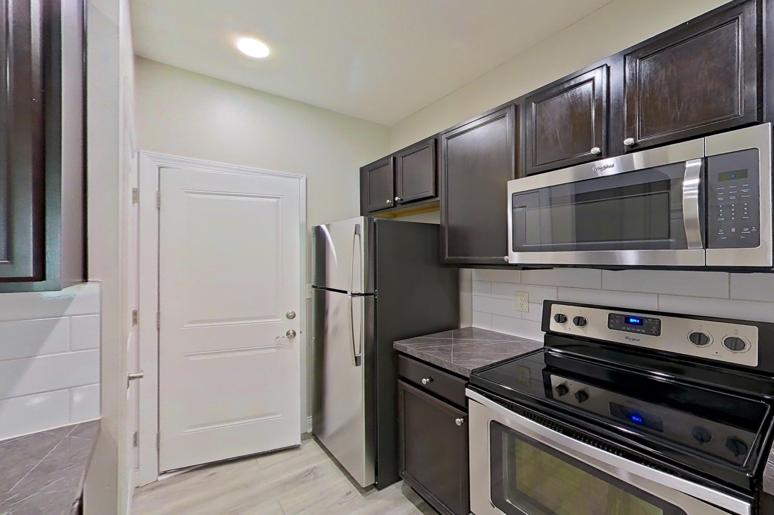 Kitchen with dark countertops, dishwasher, electric range, light countertops, light wood-finish flooring, microwave, oven/range, refrigerator, and stainless steel appliances, Apartment S9055 at Cortland Powell