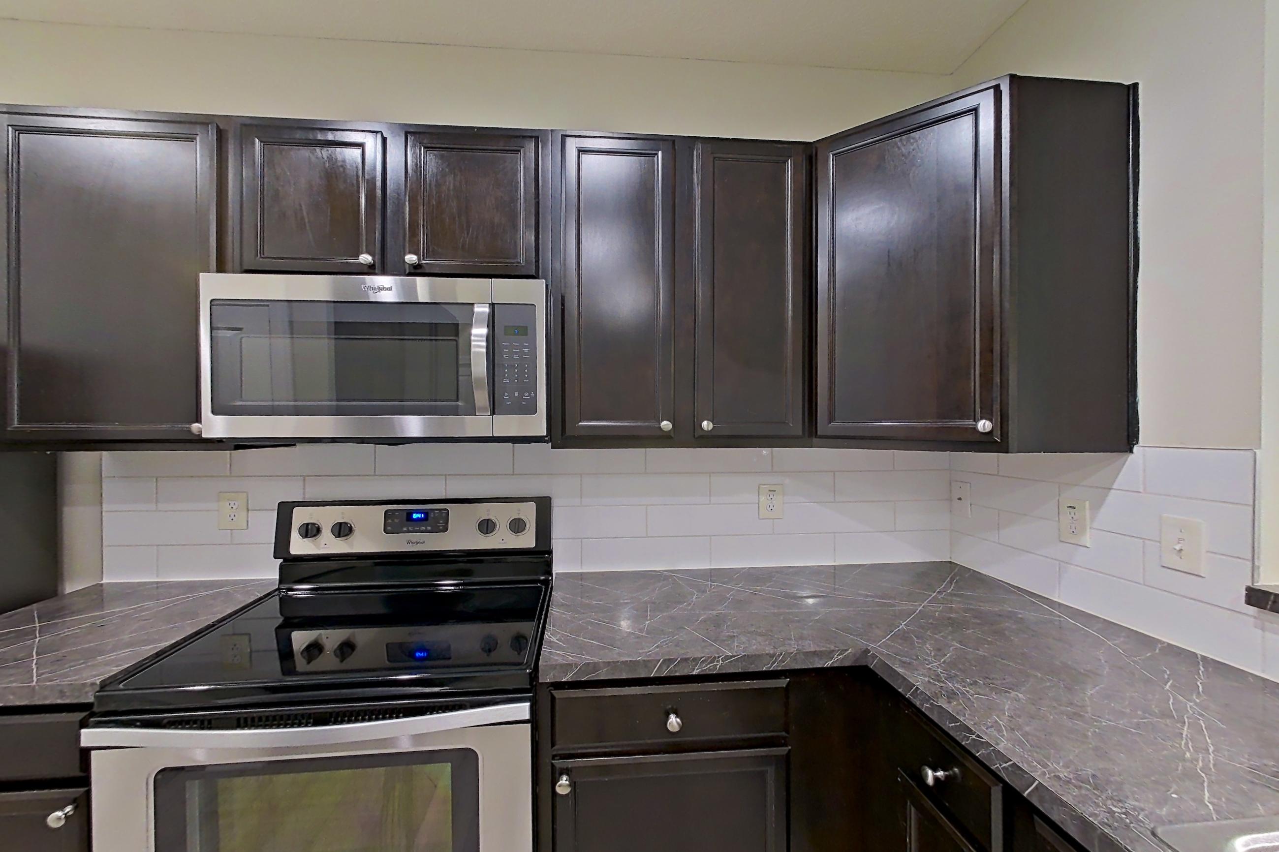 Kitchen with dark countertops, dishwasher, electric range, light countertops, light wood-finish flooring, microwave, oven/range, refrigerator, and stainless steel appliances, Apartment S9055 at Cortland Powell
