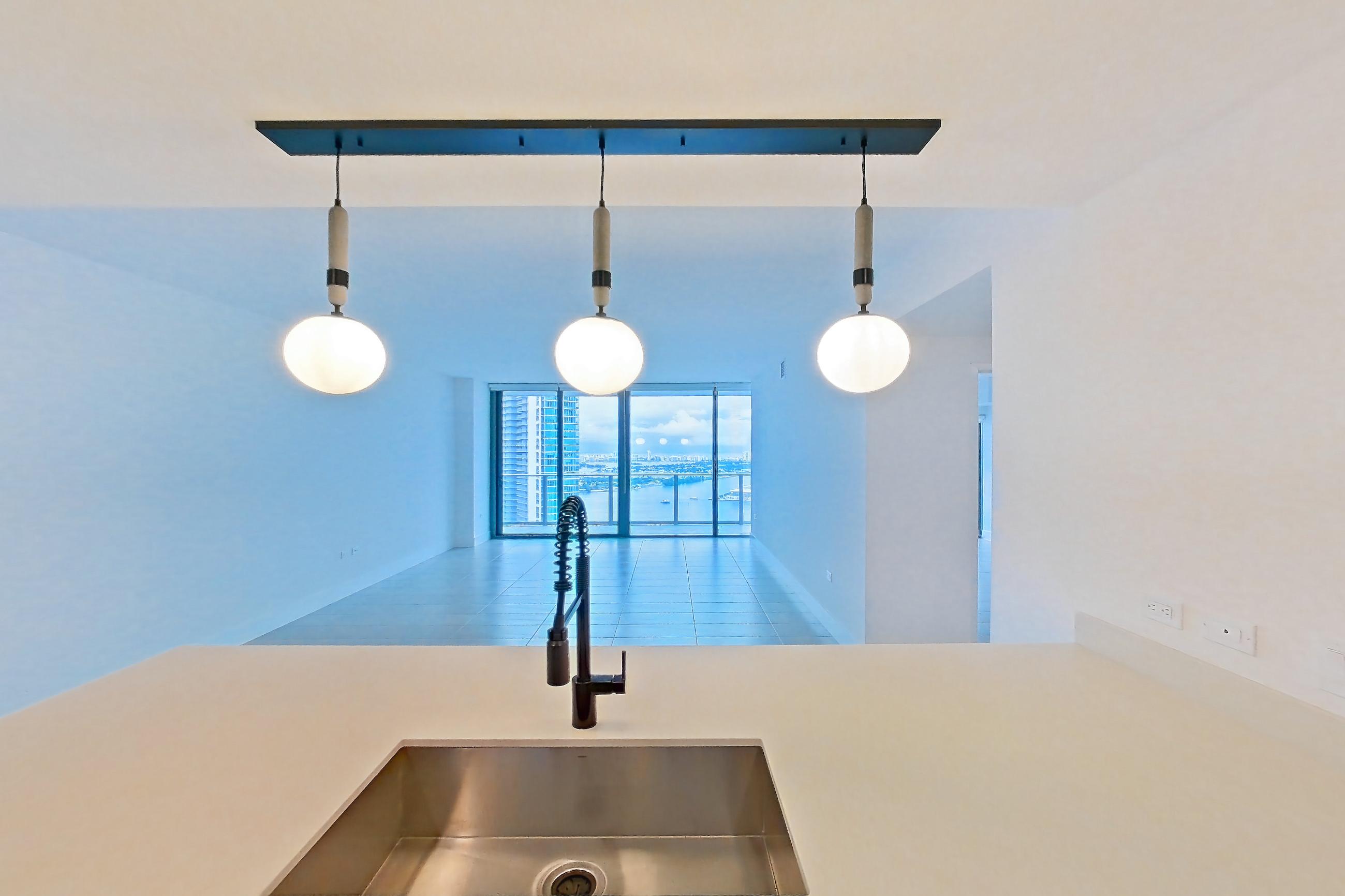 Kitchen with black appliances, cooktop, dishwasher, electric cooktop, light countertops, light tile flooring, oven/range, refrigerator, and stainless steel appliances, Apartment 4506 at Miami World Tower