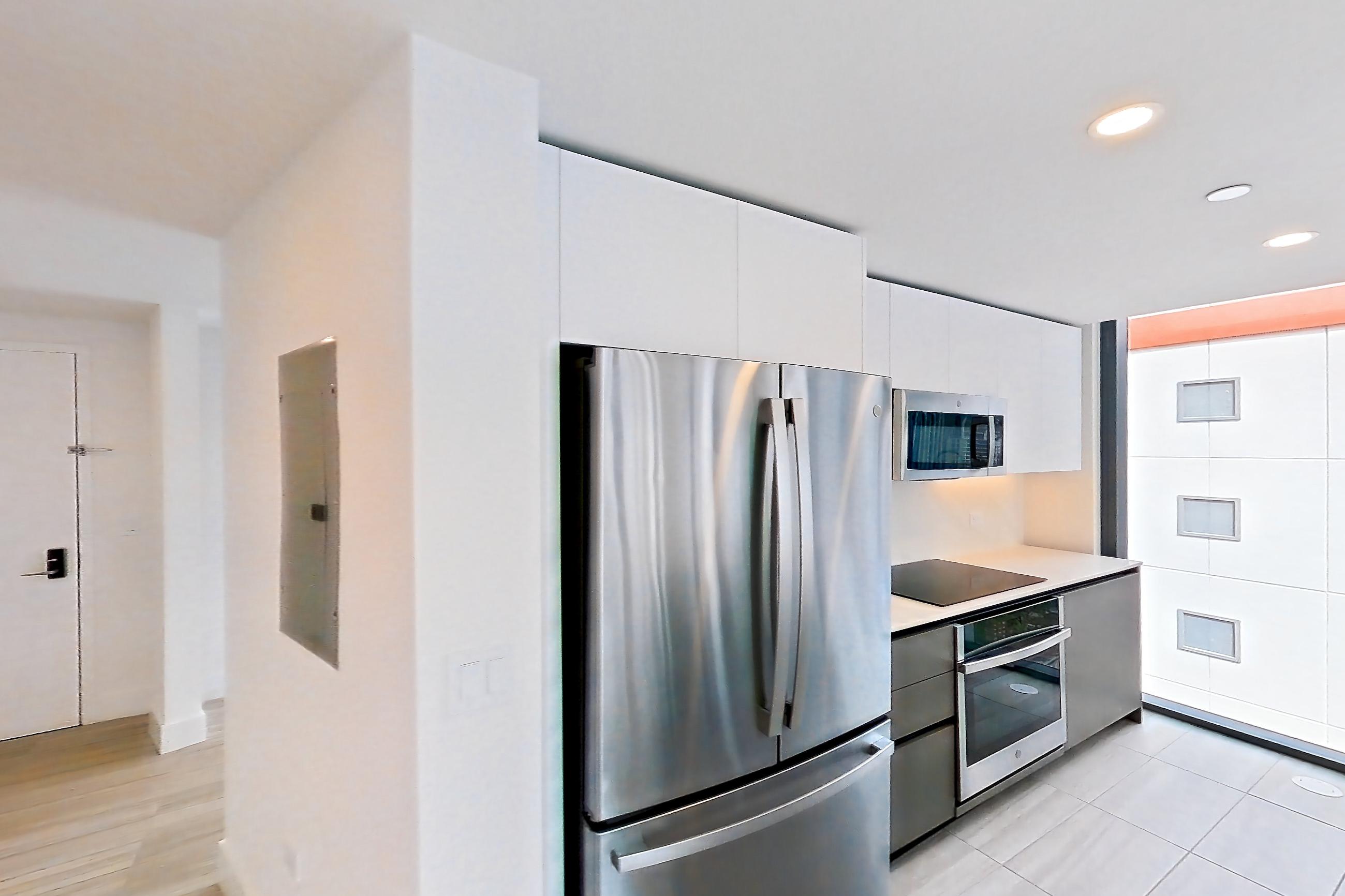 Kitchen entryway with black appliances, cooktop, electric cooktop, kitchen island, light stone countertops, light tile flooring, oven/range, refrigerator, and stainless steel appliances, Apartment 1002 at Miami World Tower