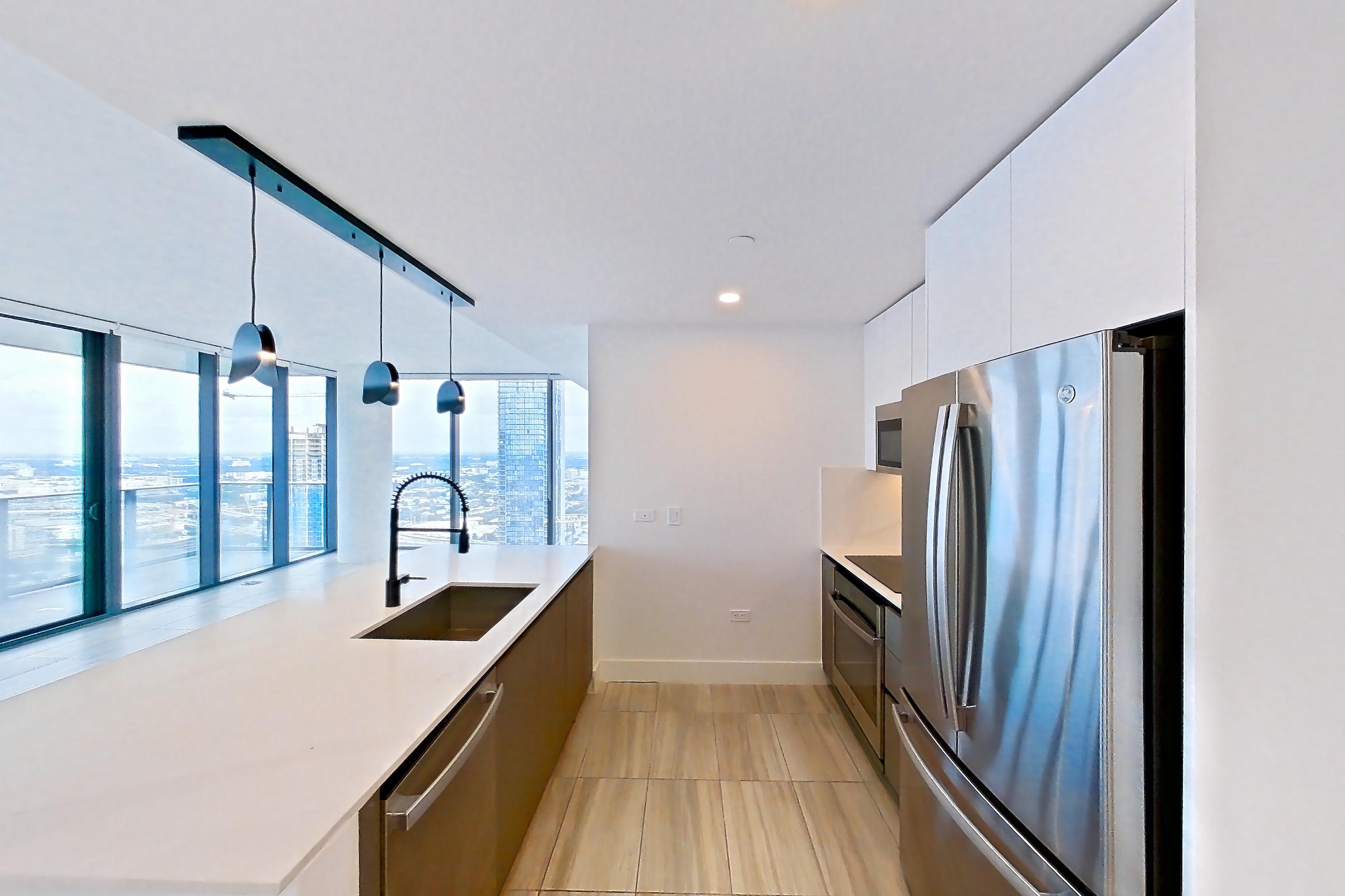 Kitchen entryway with dishwasher, kitchen island, light countertops, light stone countertops, light tile flooring, oven/range, refrigerator, and stainless steel appliances, Apartment 4401 at Miami World Tower