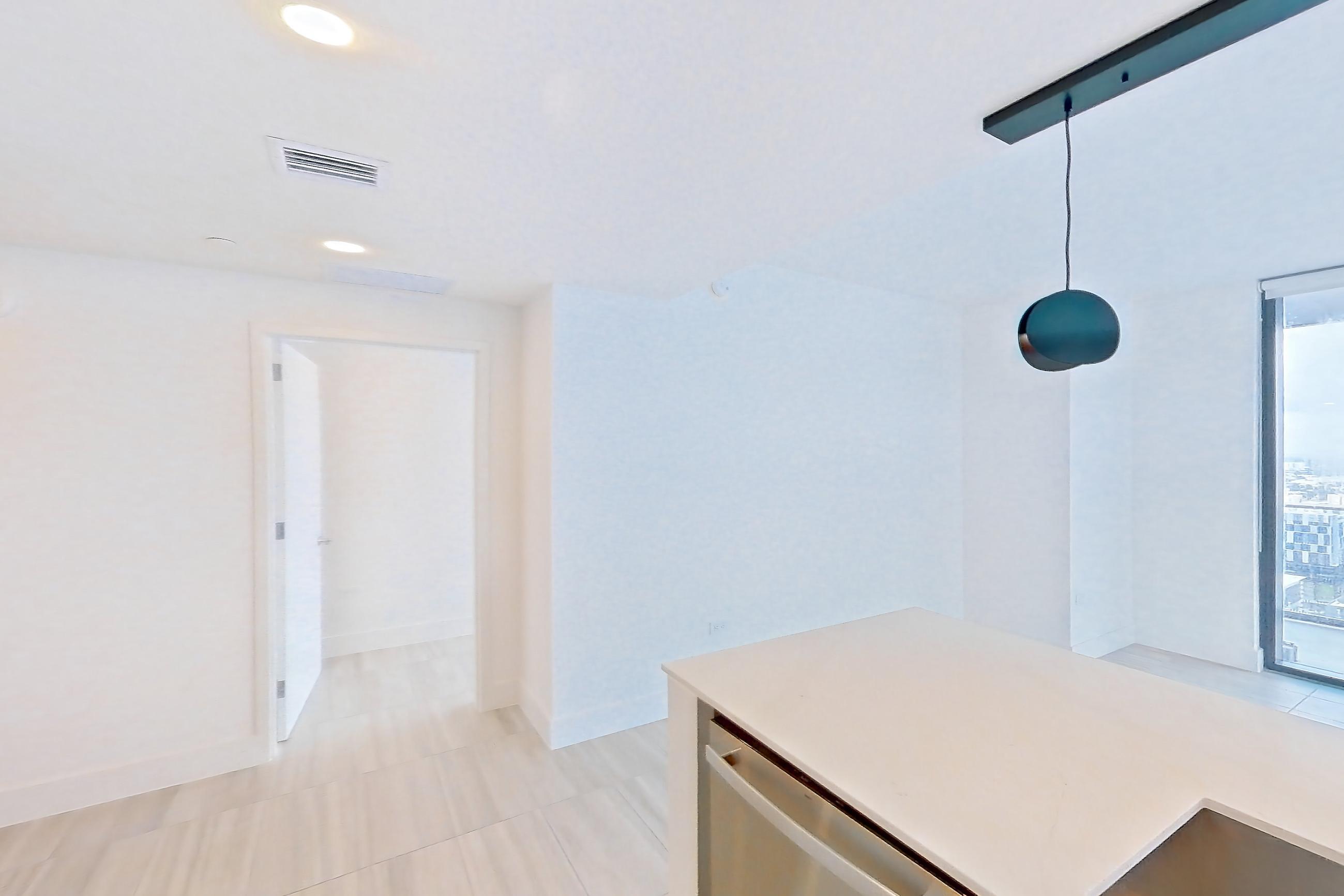 Kitchen with black appliances, cooktop, dishwasher, electric cooktop, kitchen island, light countertops, light stone countertops, light tile flooring, and stainless steel appliances, Apartment 4401 at Miami World Tower