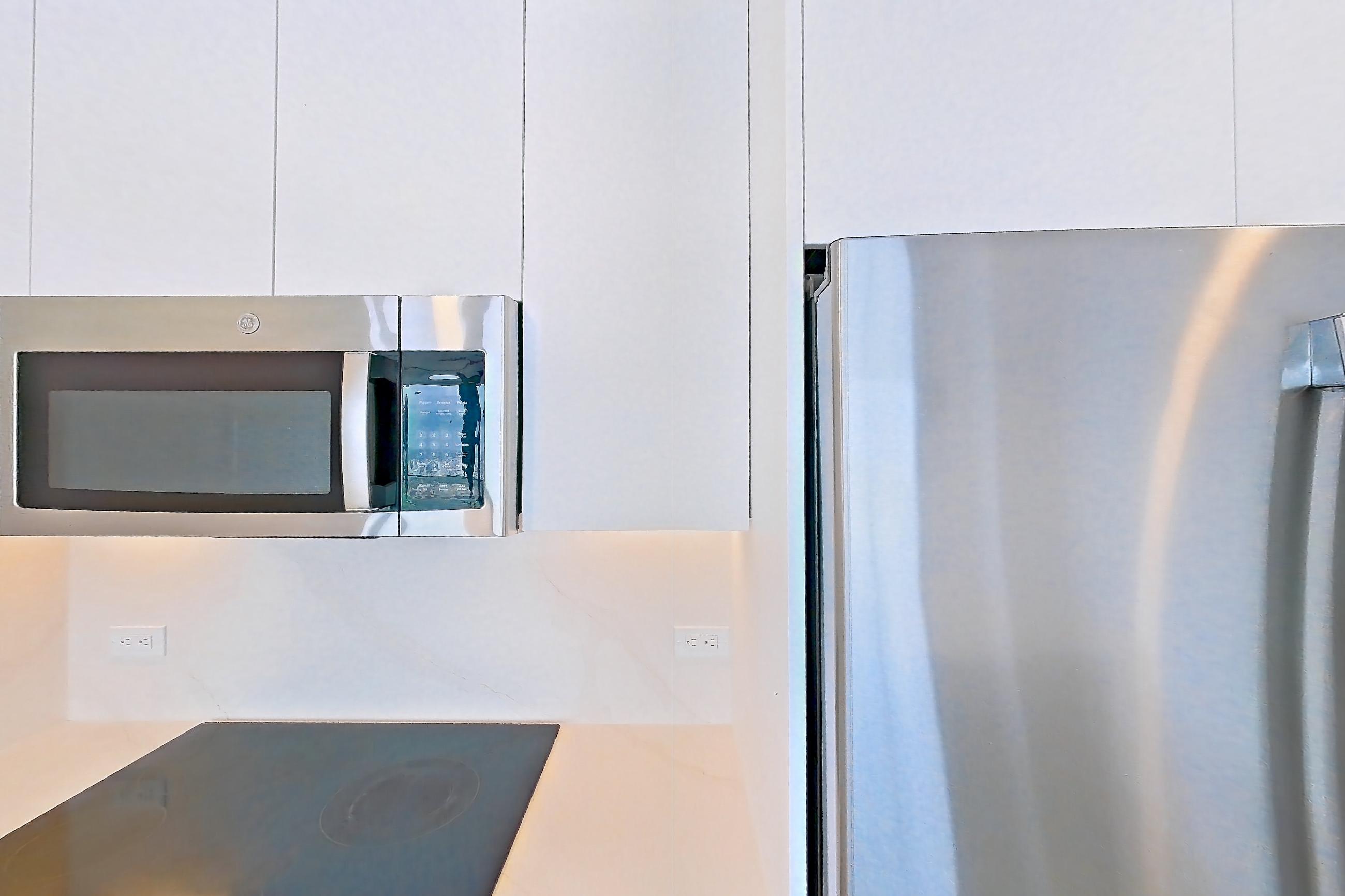 Kitchen with black appliances, cooktop, dishwasher, electric cooktop, kitchen island, light countertops, light stone countertops, light tile flooring, and stainless steel appliances, Apartment 4401 at Miami World Tower