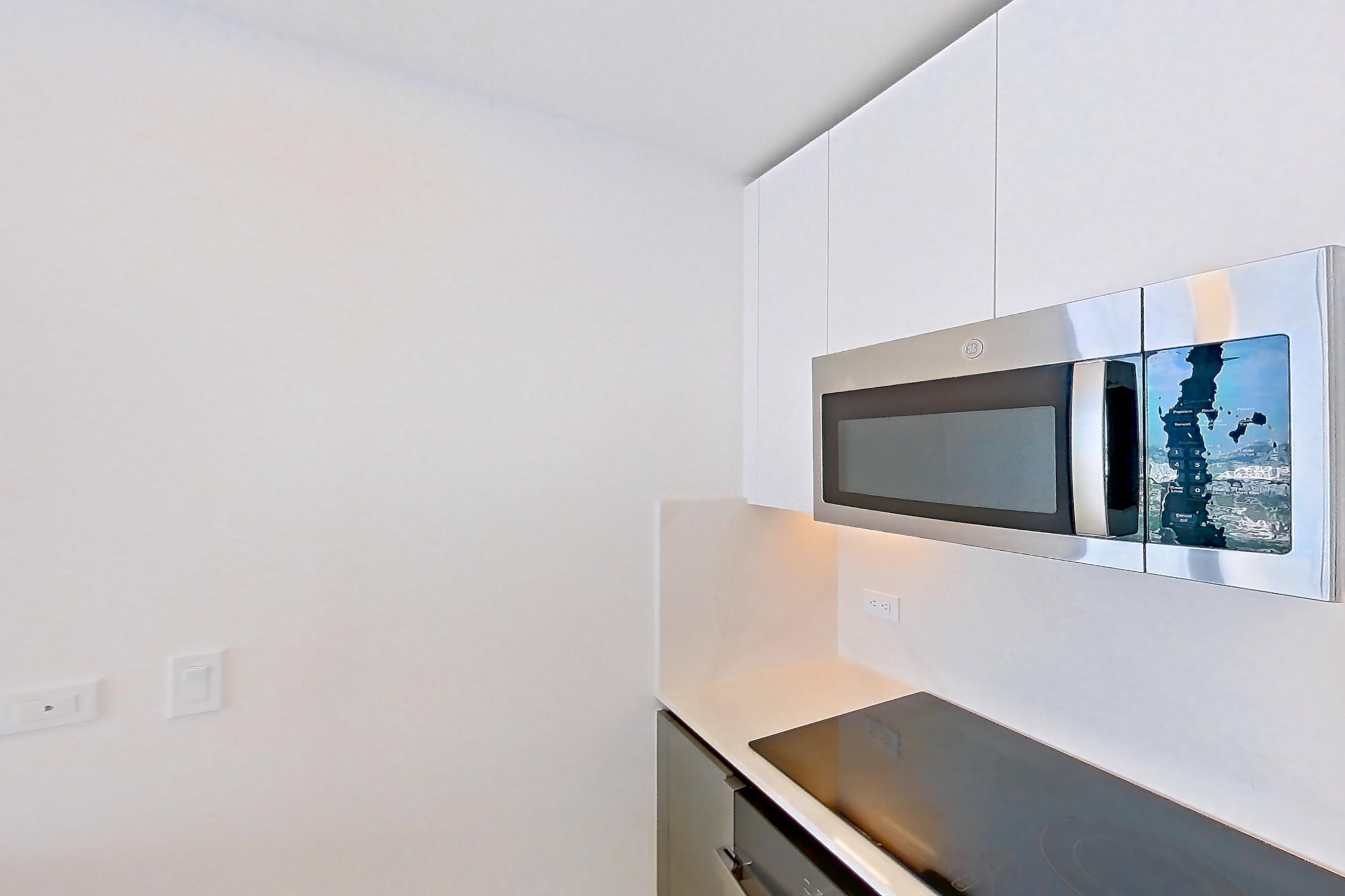Kitchen with black appliances, cooktop, dishwasher, electric cooktop, kitchen island, light stone countertops, light tile flooring, oven/range, refrigerator, and stainless steel appliances, Apartment 4601 at Miami World Tower