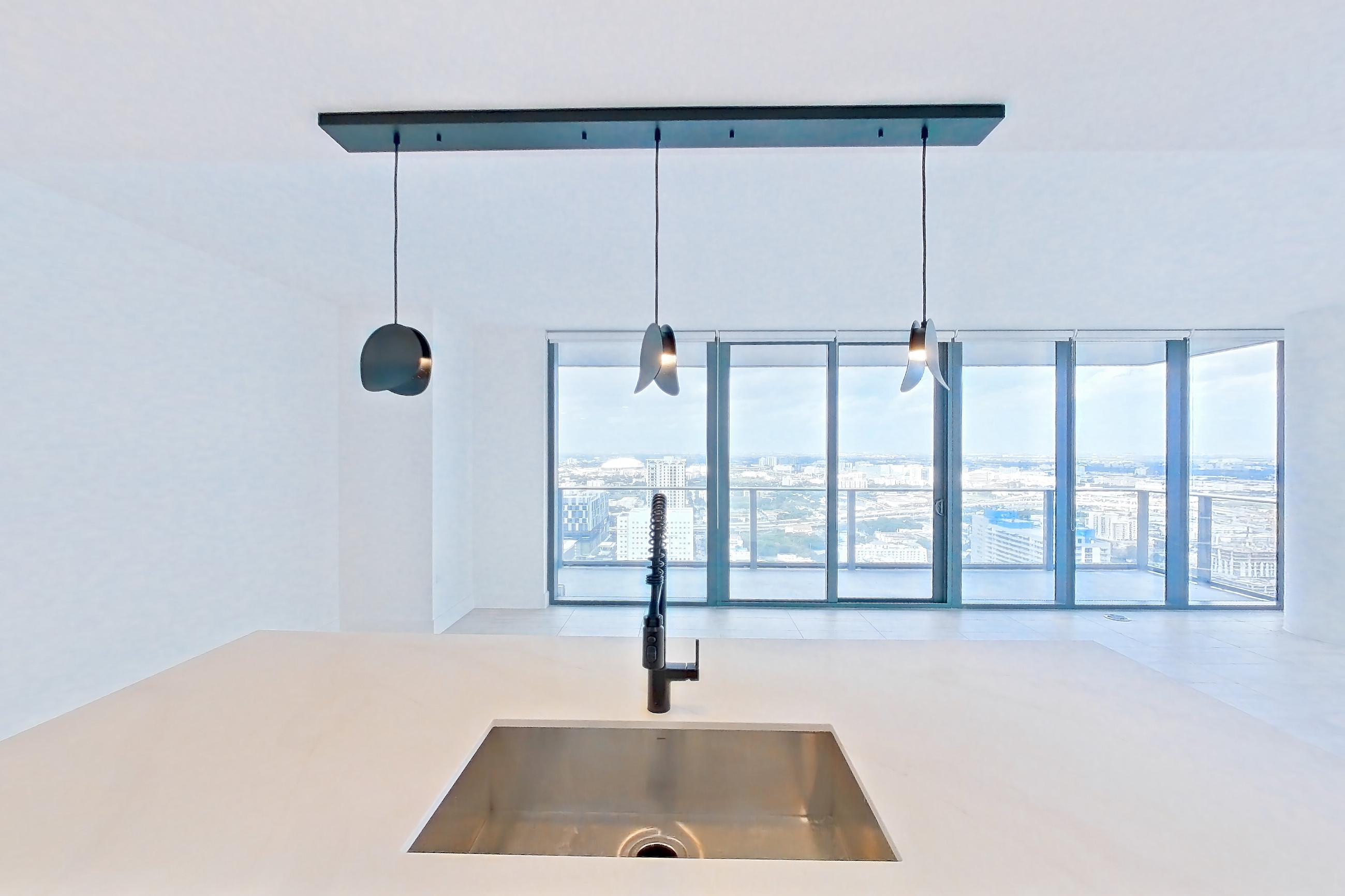Kitchen with black appliances, cooktop, dishwasher, electric cooktop, kitchen island, light stone countertops, light tile flooring, oven/range, refrigerator, and stainless steel appliances, Apartment 4601 at Miami World Tower