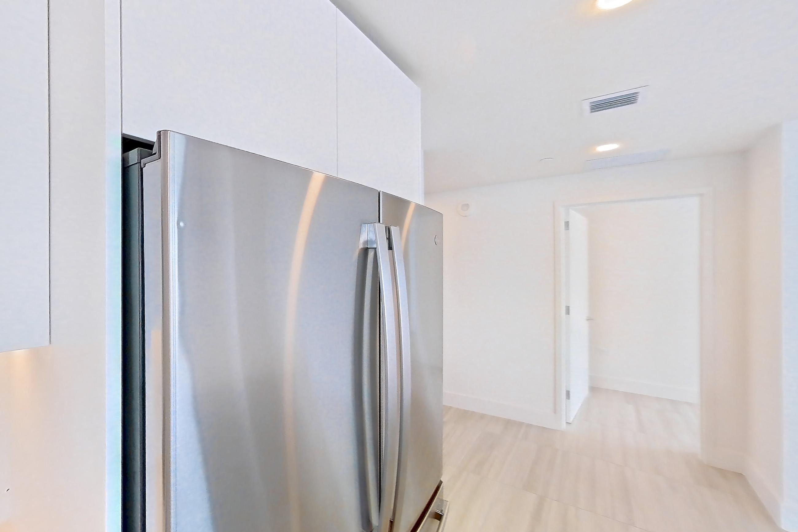 Kitchen with black appliances, cooktop, dishwasher, electric cooktop, kitchen island, light stone countertops, light tile flooring, oven/range, refrigerator, and stainless steel appliances, Apartment 4601 at Miami World Tower