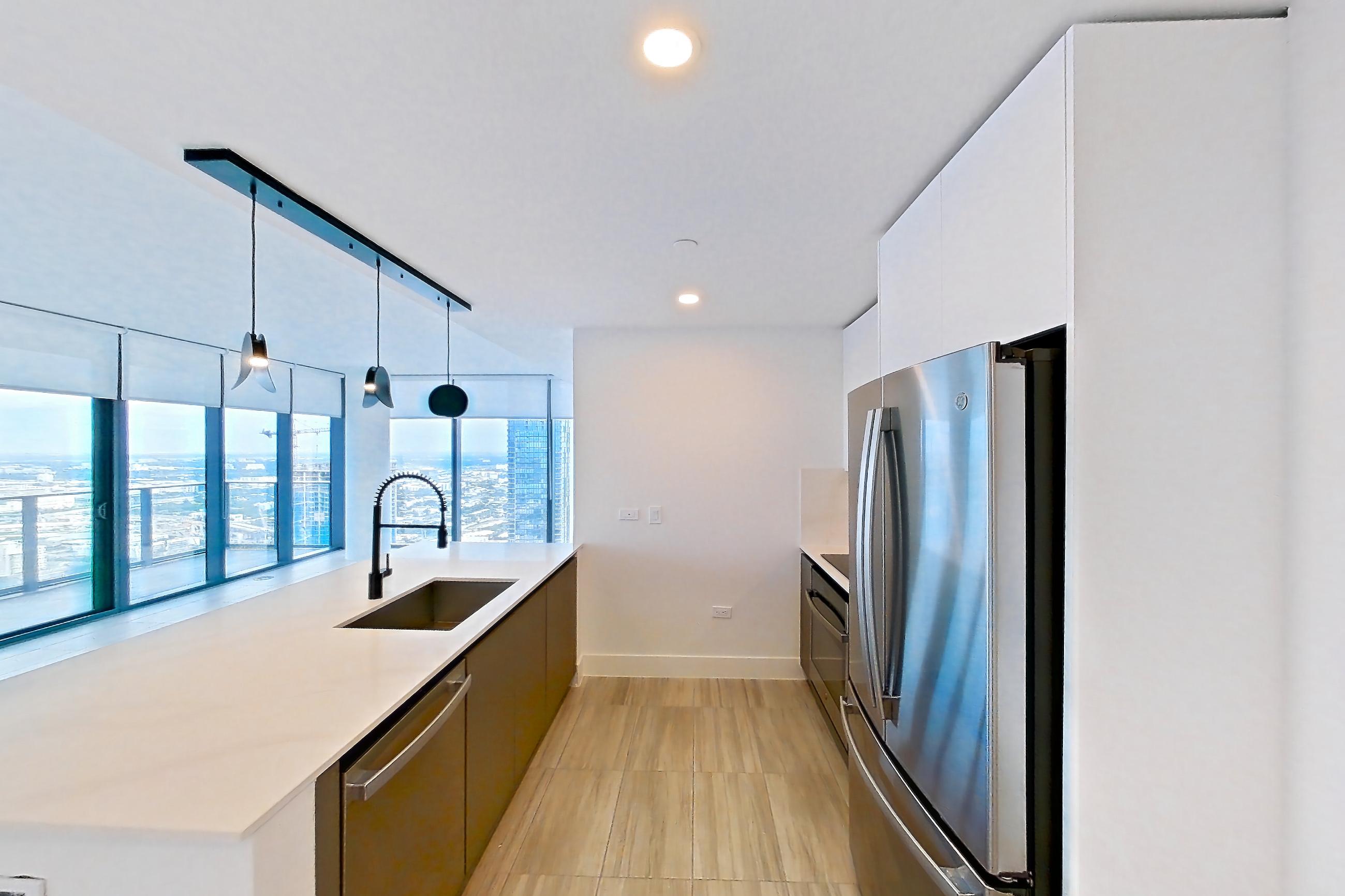 Kitchen entryway with dishwasher, light stone countertops, refrigerator, and stainless steel appliances, Apartment 5201 at Miami World Tower