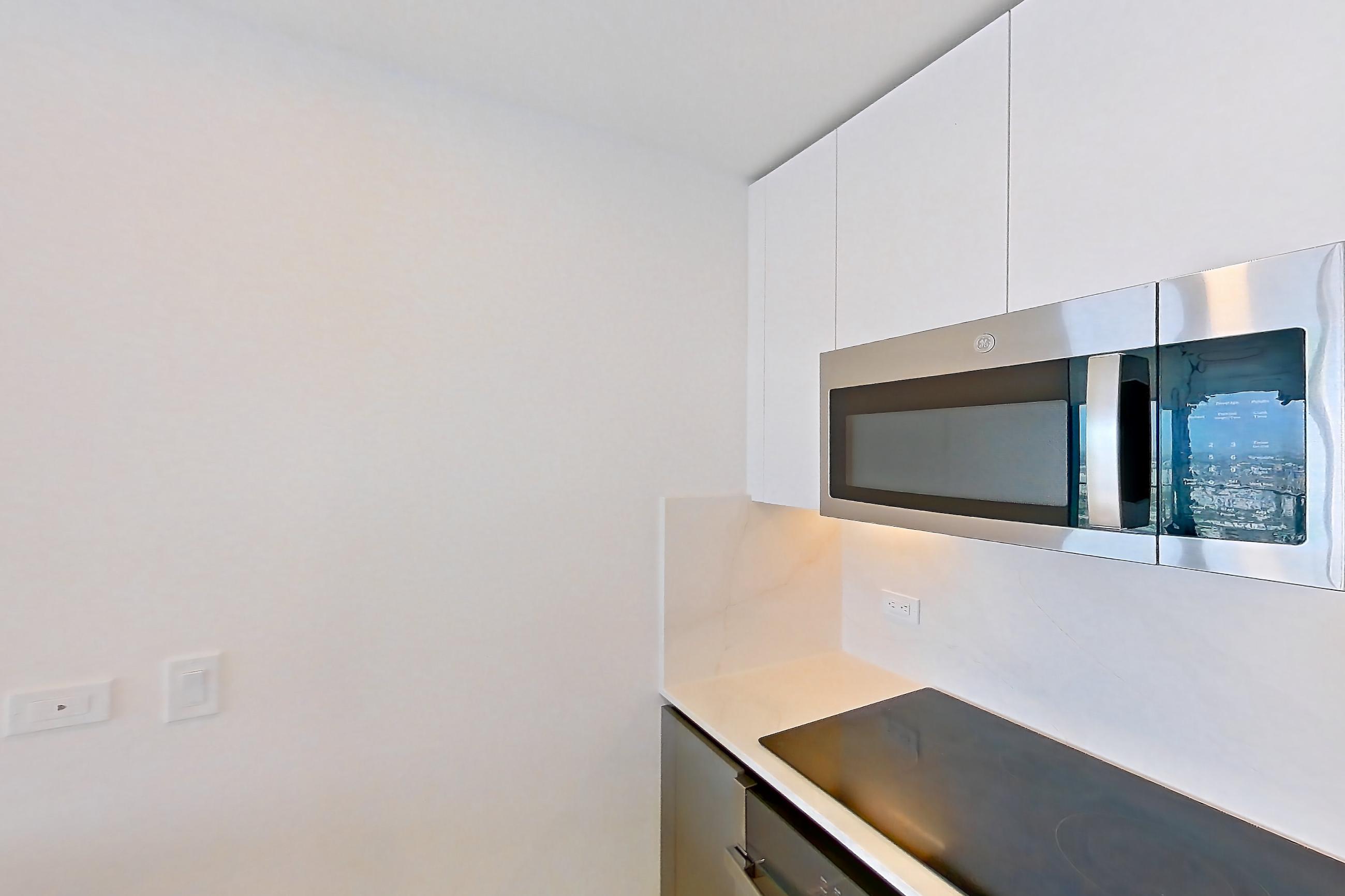 Kitchen with black appliances, cooktop, electric cooktop, kitchen island, light countertops, light stone countertops, light tile flooring, oven/range, refrigerator, and stainless steel appliances, Apartment 5201 at Miami World Tower
