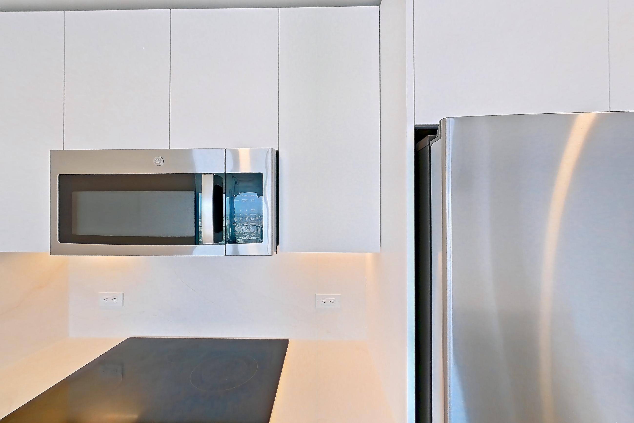 Kitchen with black appliances, cooktop, electric cooktop, kitchen island, light countertops, light stone countertops, light tile flooring, oven/range, refrigerator, and stainless steel appliances, Apartment 5201 at Miami World Tower