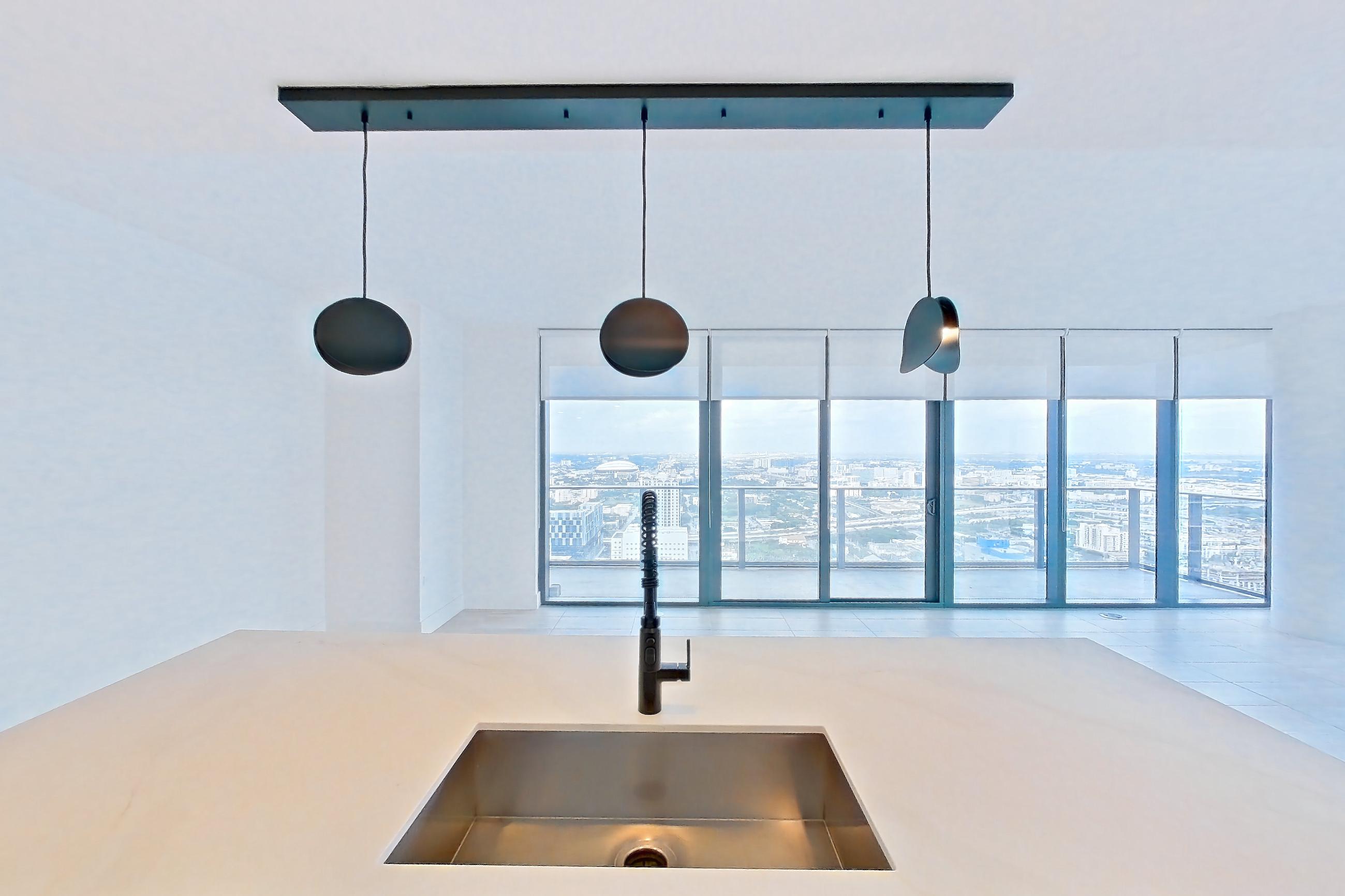 Kitchen with black appliances, cooktop, electric cooktop, kitchen island, light countertops, light stone countertops, light tile flooring, oven/range, refrigerator, and stainless steel appliances, Apartment 5201 at Miami World Tower