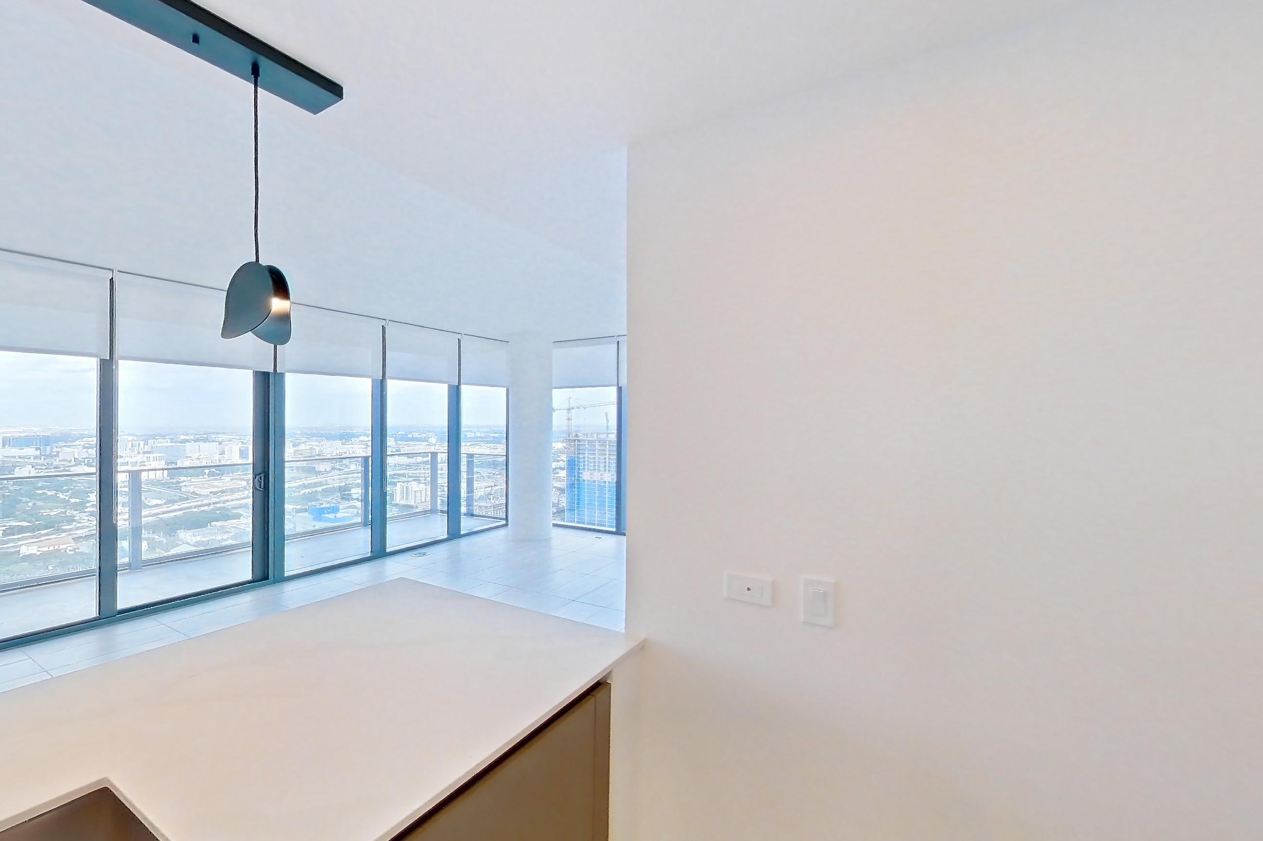 Kitchen with black appliances, cooktop, electric cooktop, kitchen island, light countertops, light stone countertops, light tile flooring, oven/range, refrigerator, and stainless steel appliances, Apartment 5201 at Miami World Tower