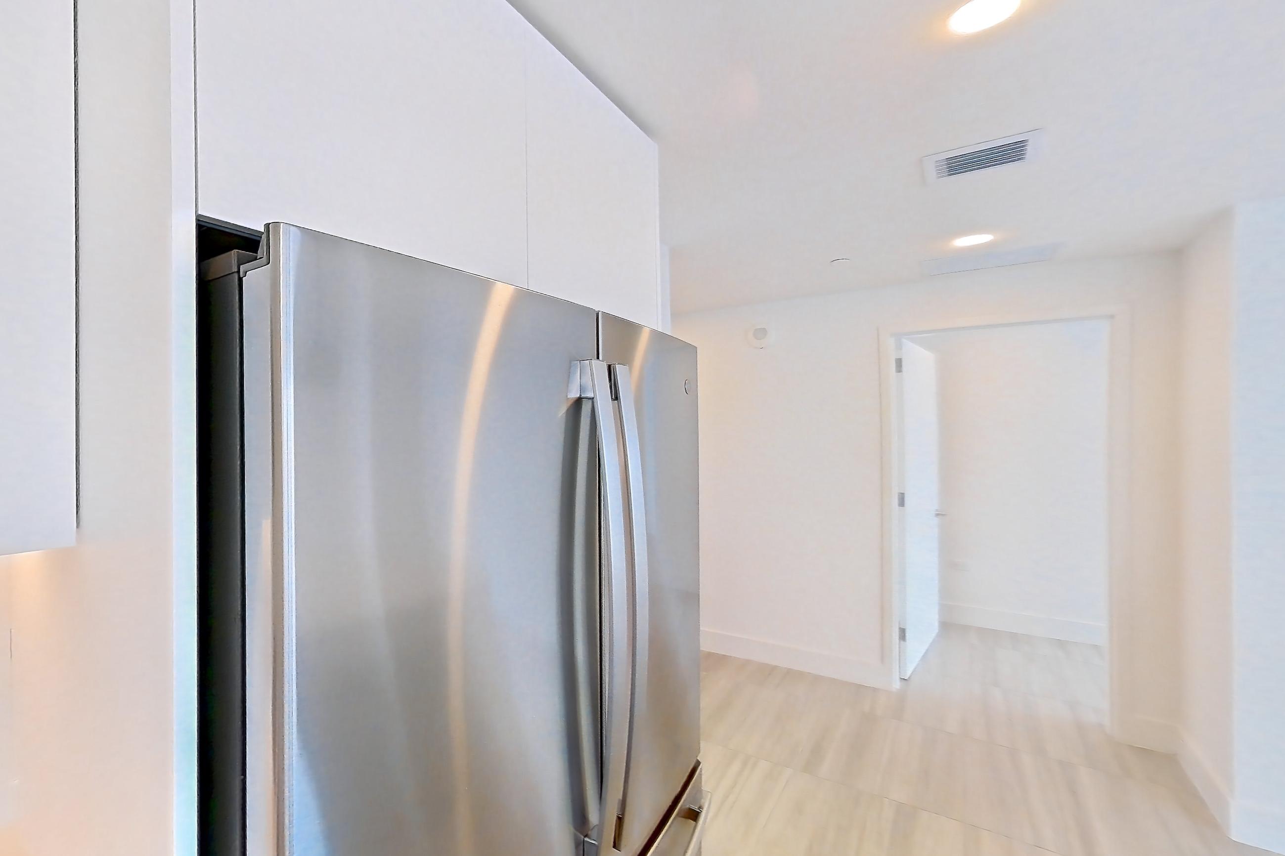 Kitchen with black appliances, cooktop, electric cooktop, kitchen island, light countertops, light stone countertops, light tile flooring, oven/range, refrigerator, and stainless steel appliances, Apartment 5201 at Miami World Tower