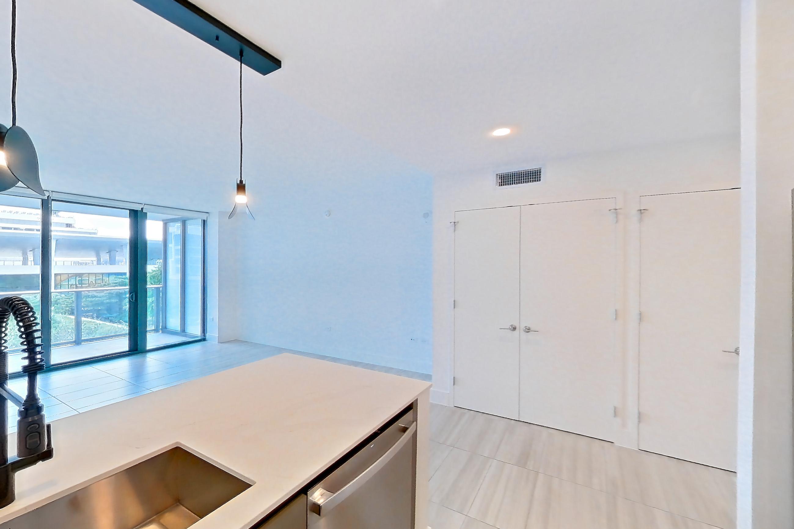 Kitchen with black appliances, cooktop, dishwasher, electric cooktop, light countertops, light stone countertops, light tile flooring, refrigerator, and stainless steel appliances, Apartment 0608 at Miami World Tower