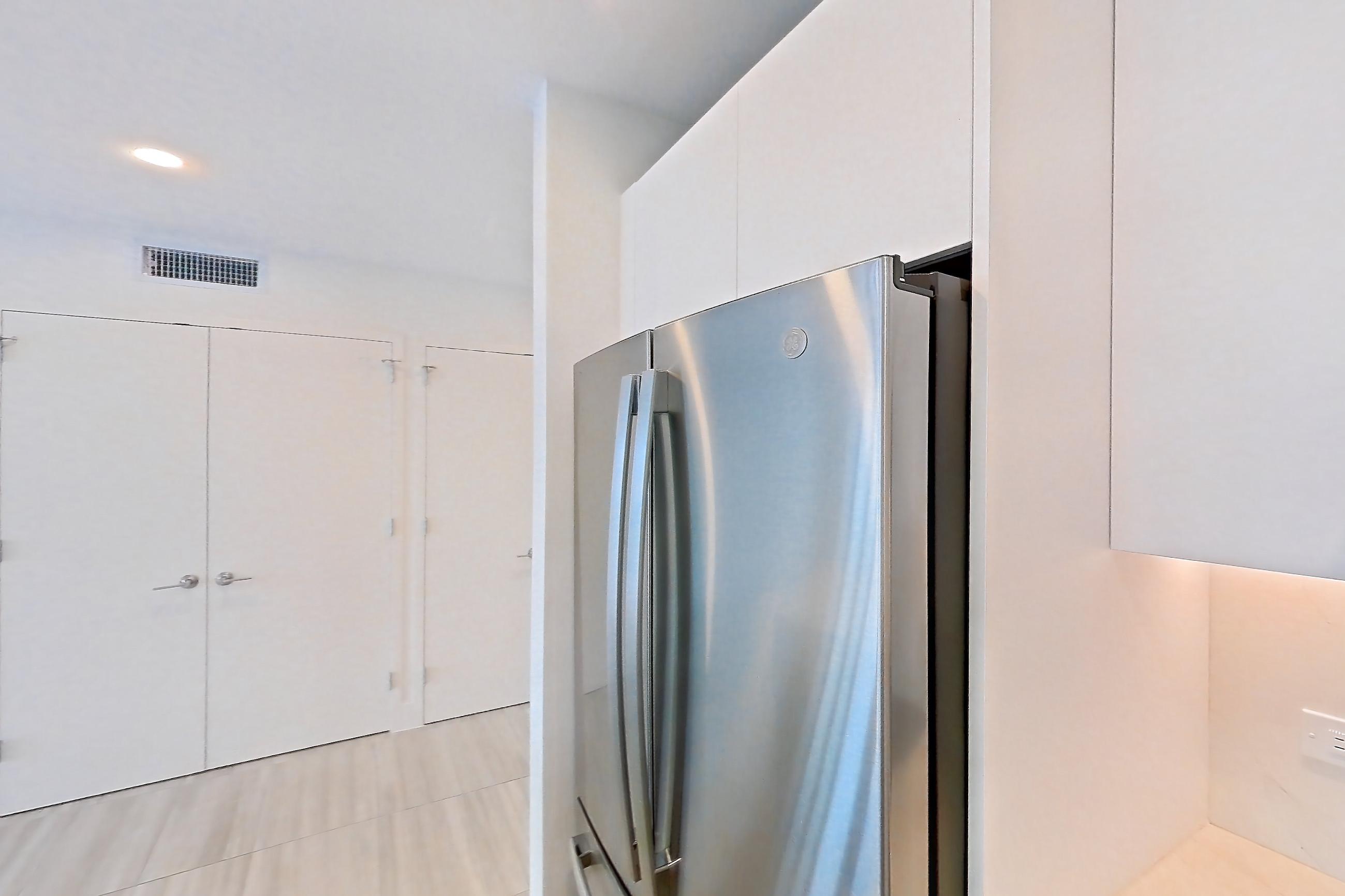 Kitchen with black appliances, cooktop, dishwasher, electric cooktop, light countertops, light stone countertops, light tile flooring, refrigerator, and stainless steel appliances, Apartment 0608 at Miami World Tower