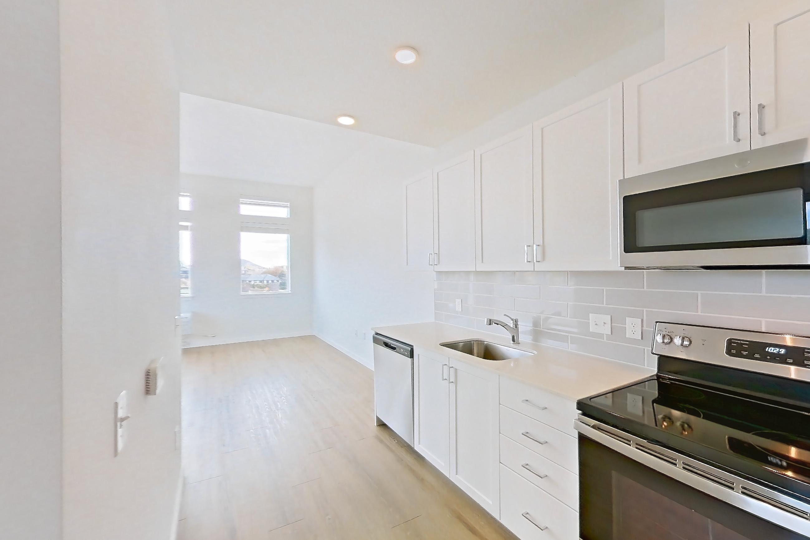 Kitchen with electric range, light countertops, light stone countertops, light wood-finish flooring, microwave, oven/range, refrigerator, and stainless steel appliances, Apartment 335 at The Eddy Apartments