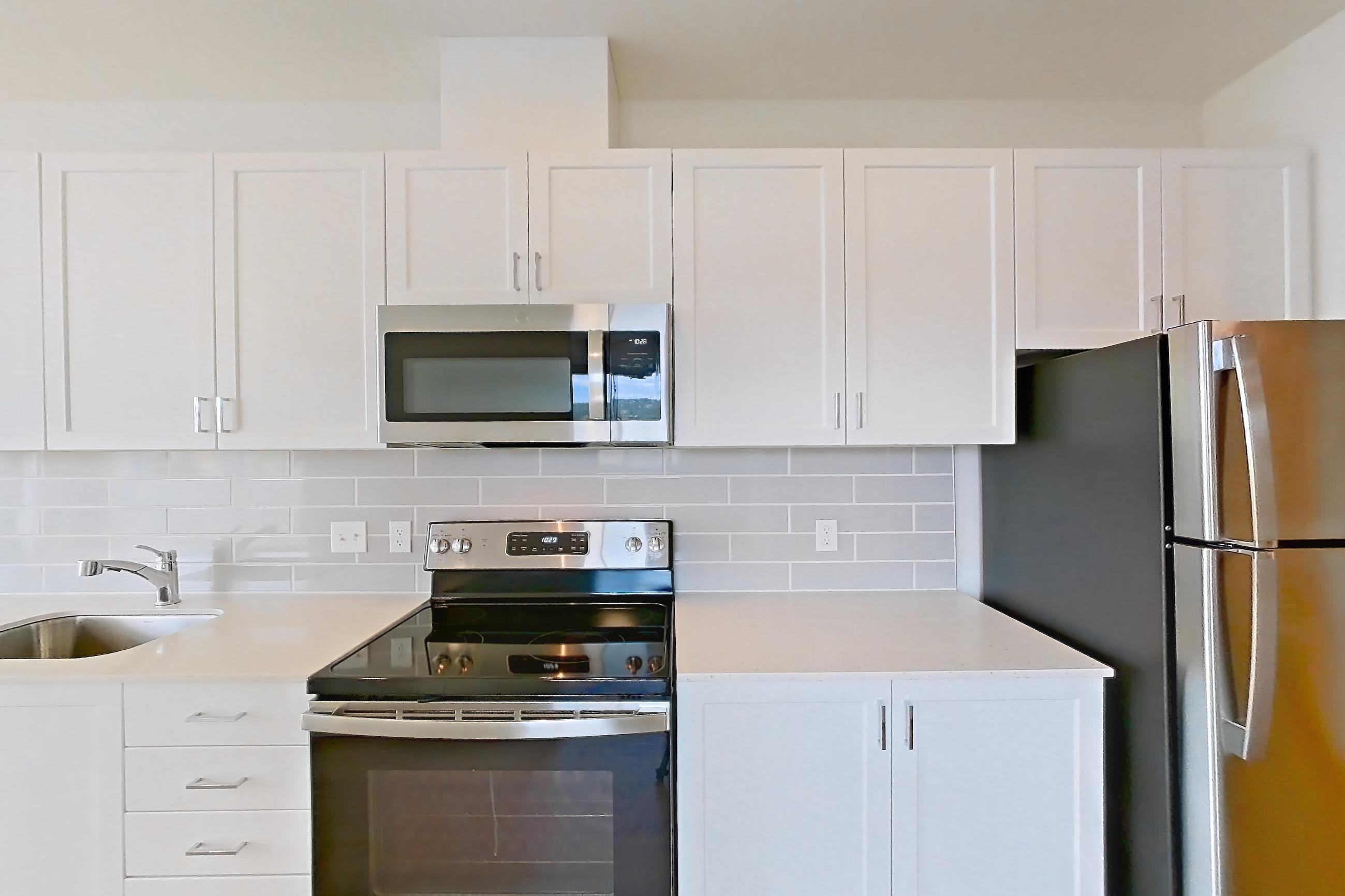 Kitchen with electric range, light countertops, light stone countertops, light wood-finish flooring, microwave, oven/range, refrigerator, and stainless steel appliances, Apartment 335 at The Eddy Apartments