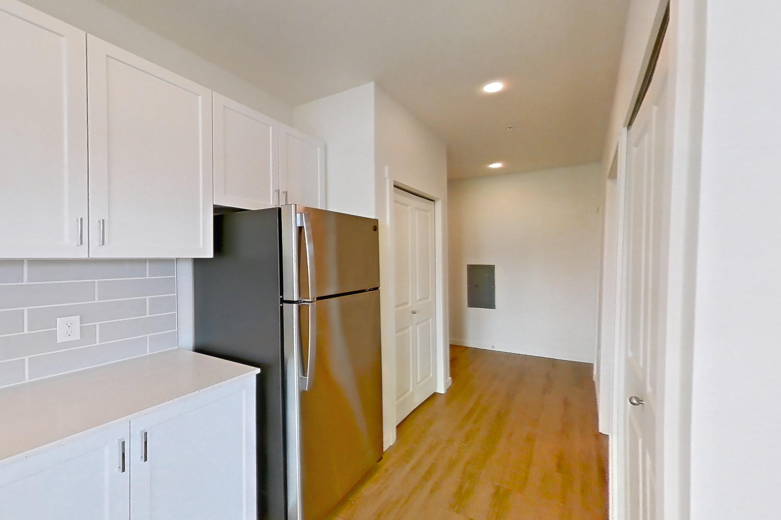 Kitchen with electric range, light countertops, light stone countertops, light wood-finish flooring, microwave, oven/range, refrigerator, and stainless steel appliances, Apartment 335 at The Eddy Apartments