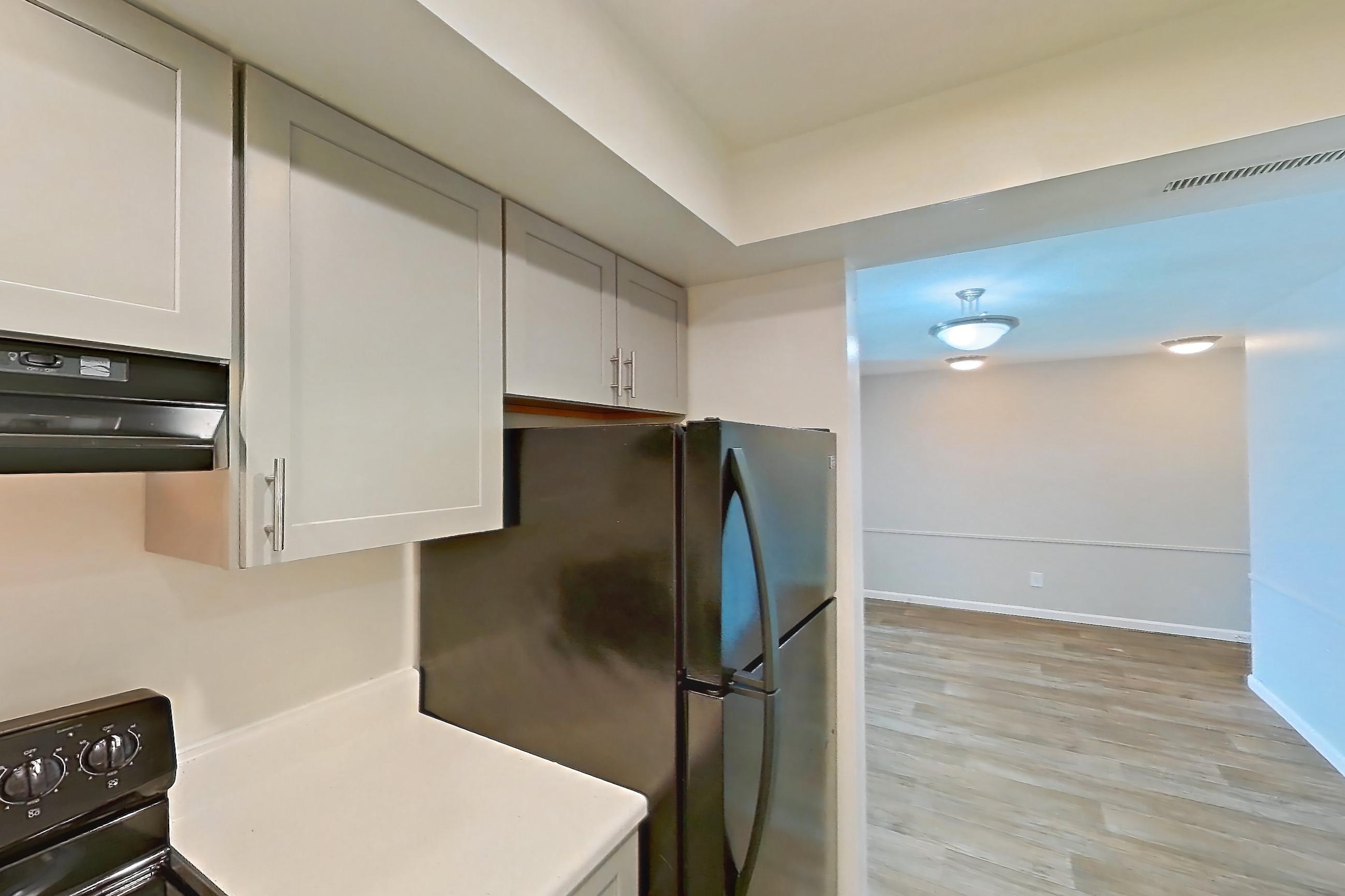 Kitchen with black appliances, dishwasher, electric range, light countertops, light wood-finish flooring, oven/range, refrigerator, and stainless steel appliances, Apartment 5201-2 at Canterbury Green