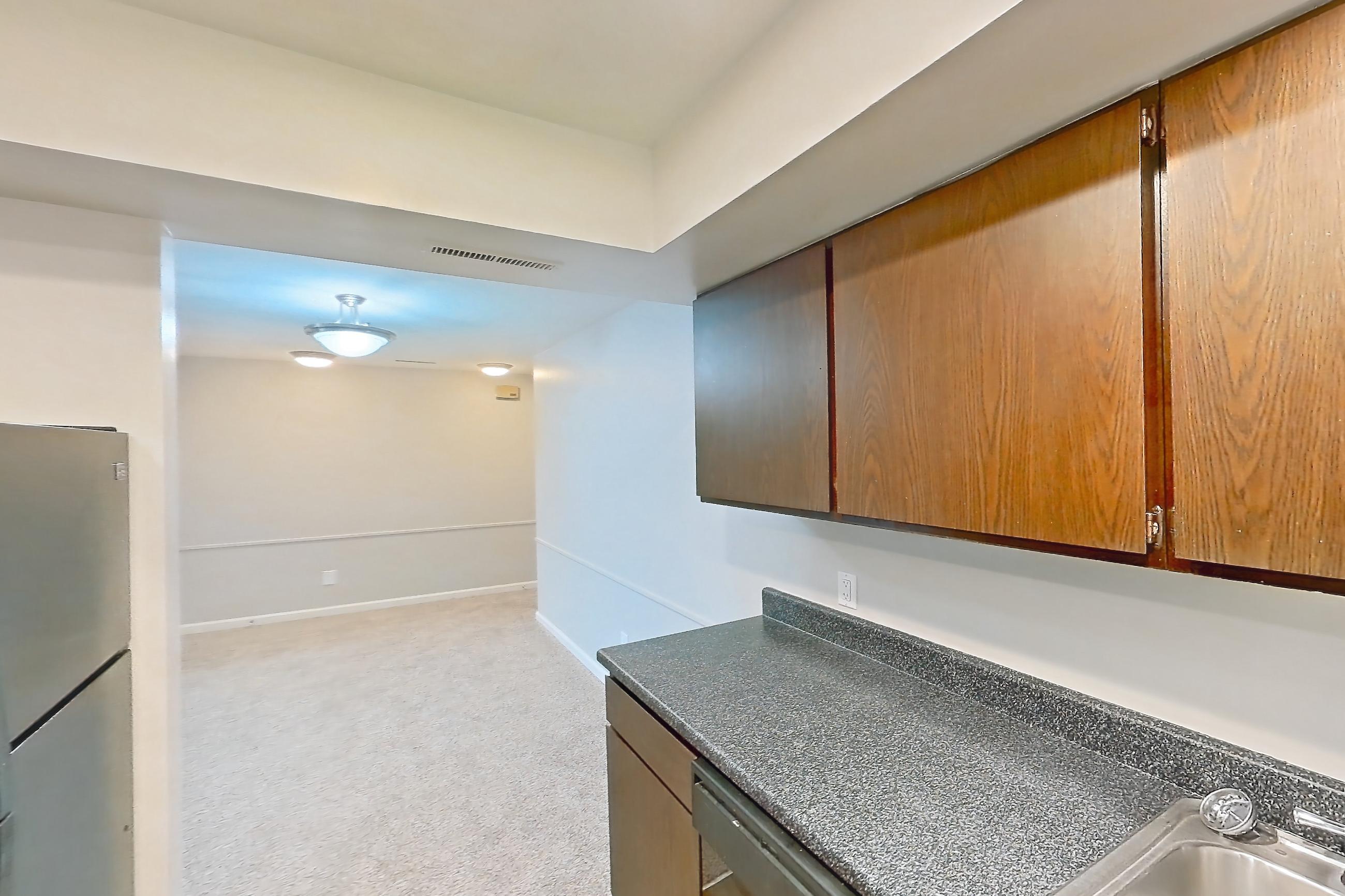 Kitchen with black appliances, dark countertops, electric range, light carpet, light wood-finish flooring, oven/range, refrigerator, and stainless steel appliances, Apartment 5630-6 at Canterbury Green