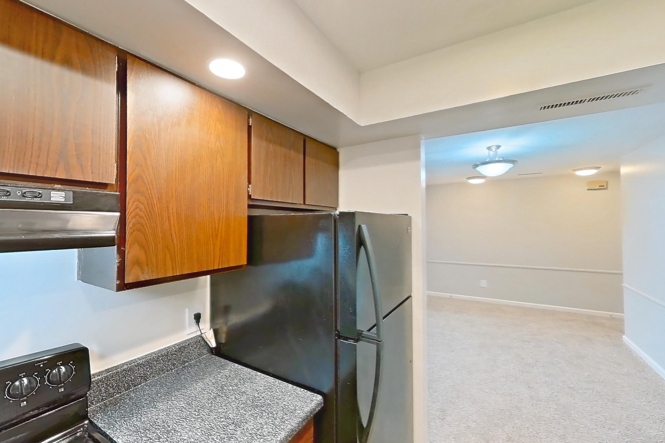 Kitchen with black appliances, dark countertops, electric range, light carpet, light wood-finish flooring, oven/range, refrigerator, and stainless steel appliances, Apartment 5630-6 at Canterbury Green
