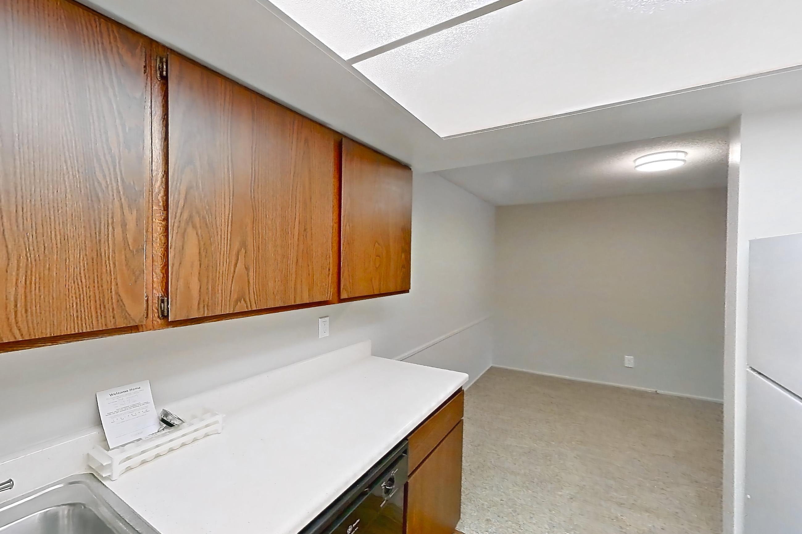 Kitchen with black appliances, dishwasher, electric range, light carpet, light countertops, light wood-finish flooring, oven/range, refrigerator, and white appliances, Apartment 5612-2ST at Canterbury Green