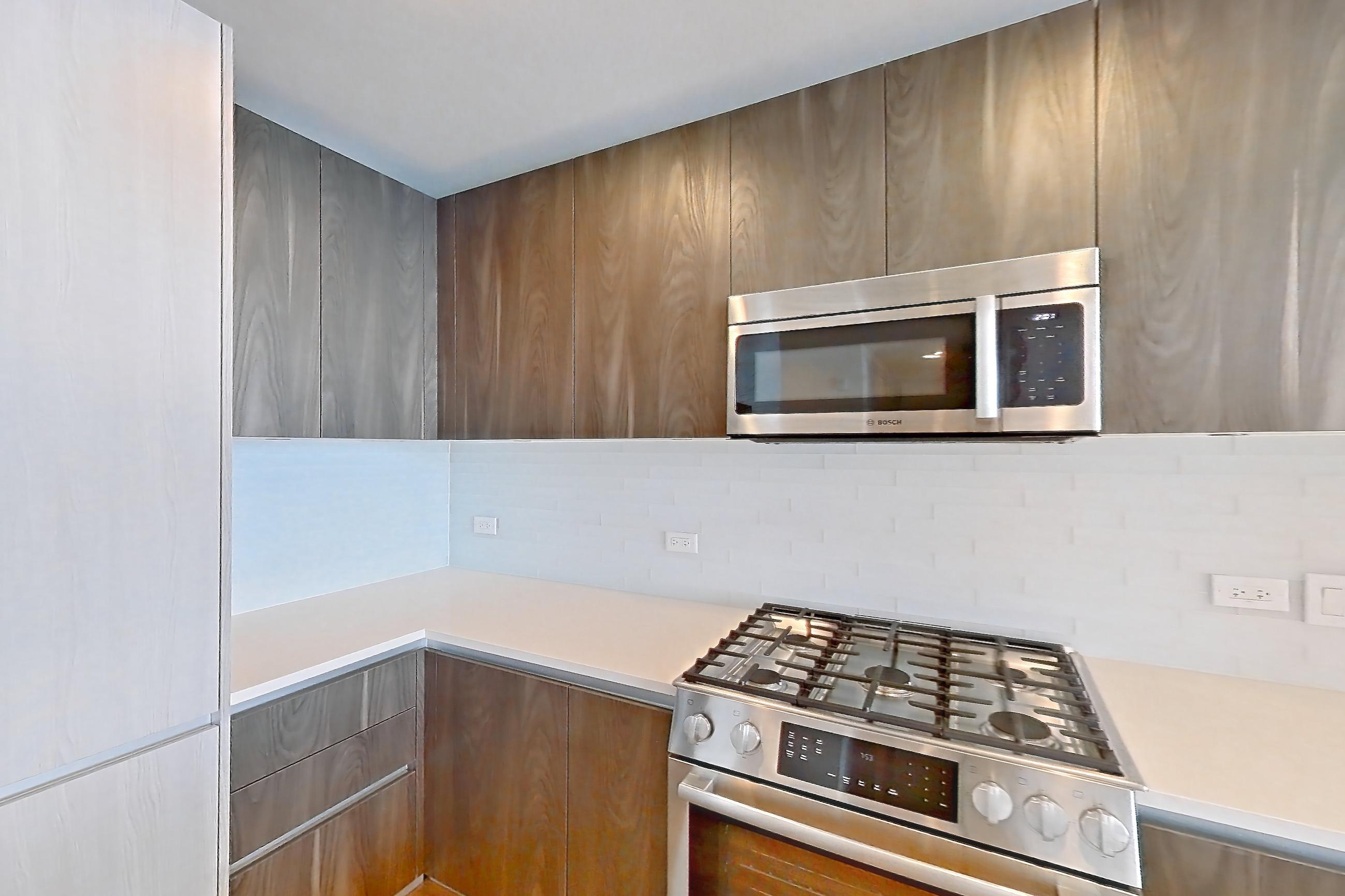 Kitchen with dishwasher, gas range, light countertops, light stone countertops, light wood-finish flooring, microwave, oven/range, stainless steel appliances, and wood-finish flooring, Apartment 1102 at The Residences at La Colombe d'Or
