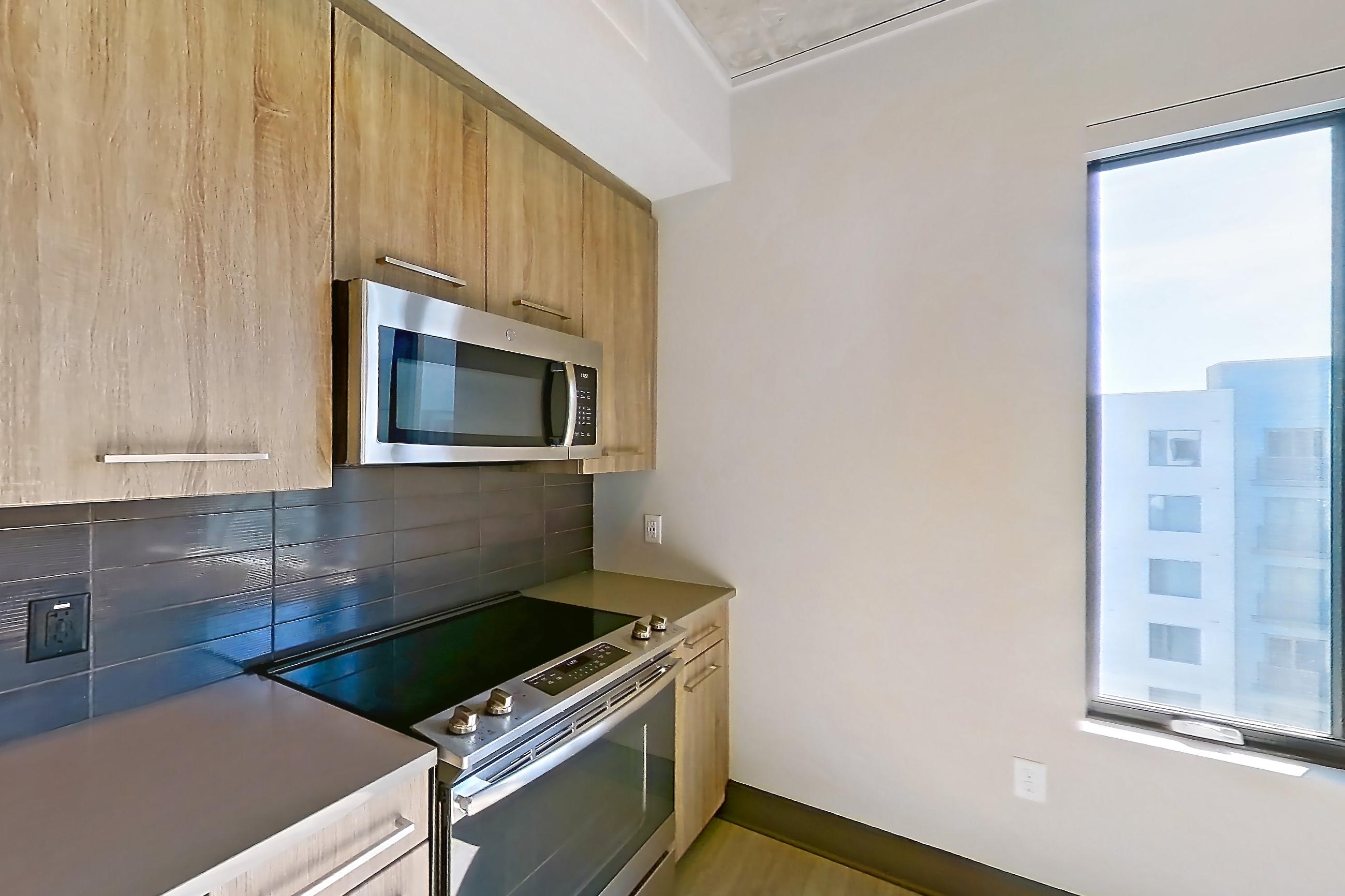 Kitchen with dark countertops, dishwasher, electric range, light wood-finish flooring, oven/range, refrigerator, and stainless steel appliances, Apartment 1105 at Cortland Glenwood South