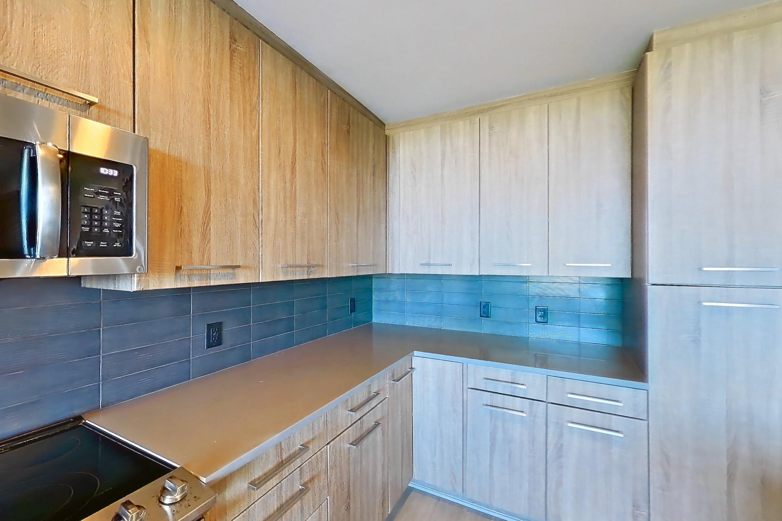 Kitchen with dark countertops, dishwasher, electric range, light countertops, light stone countertops, light wood-finish flooring, microwave, oven/range, refrigerator, stainless steel appliances, and water & ice dispenser, Apartment 1108 at Cortland Glenwood South